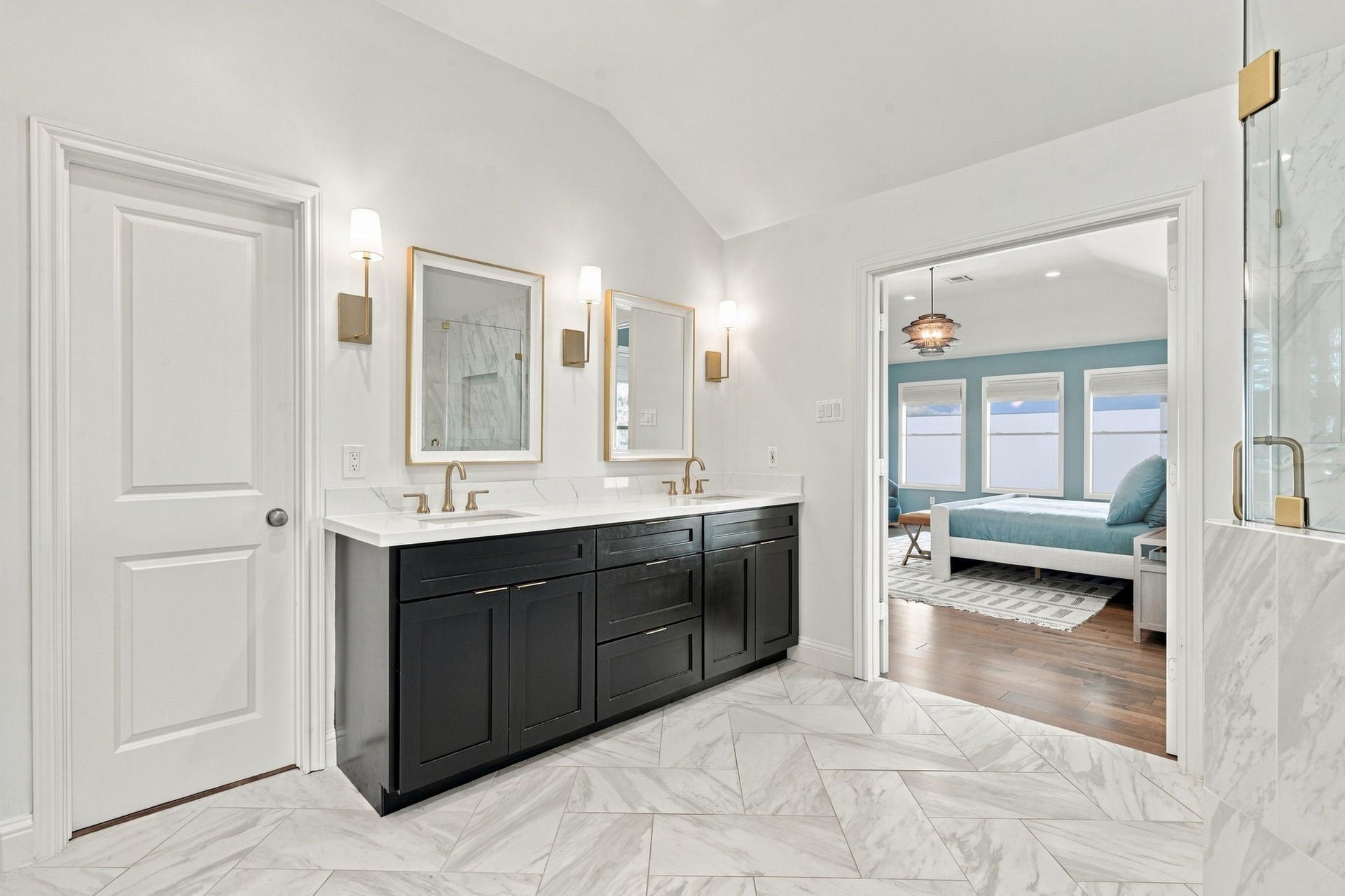 Additional view of the primary bath showcasing the expansive dual-sink vanity w/quartz countertops, dark cabinetry, gold fixtures & individual mirrors accented by stylish wall sconces.