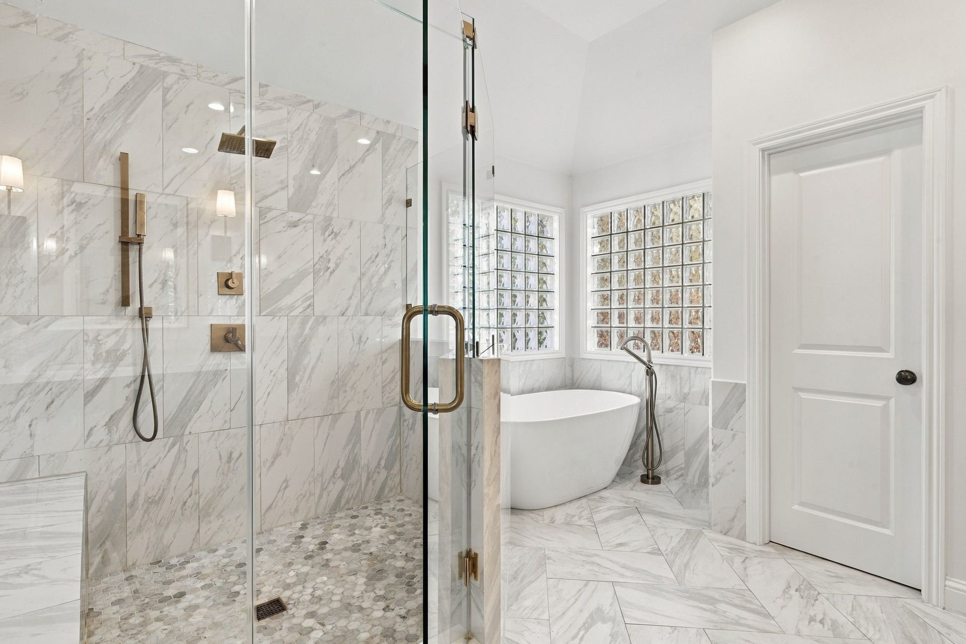 Closer look at the impressive glass-enclosed shower w/marble-look tile, rainfall showerhead, handheld shower fixture & built-in bench. Freestanding soaking tub is surrounded by glass block windows that bring in natural light.