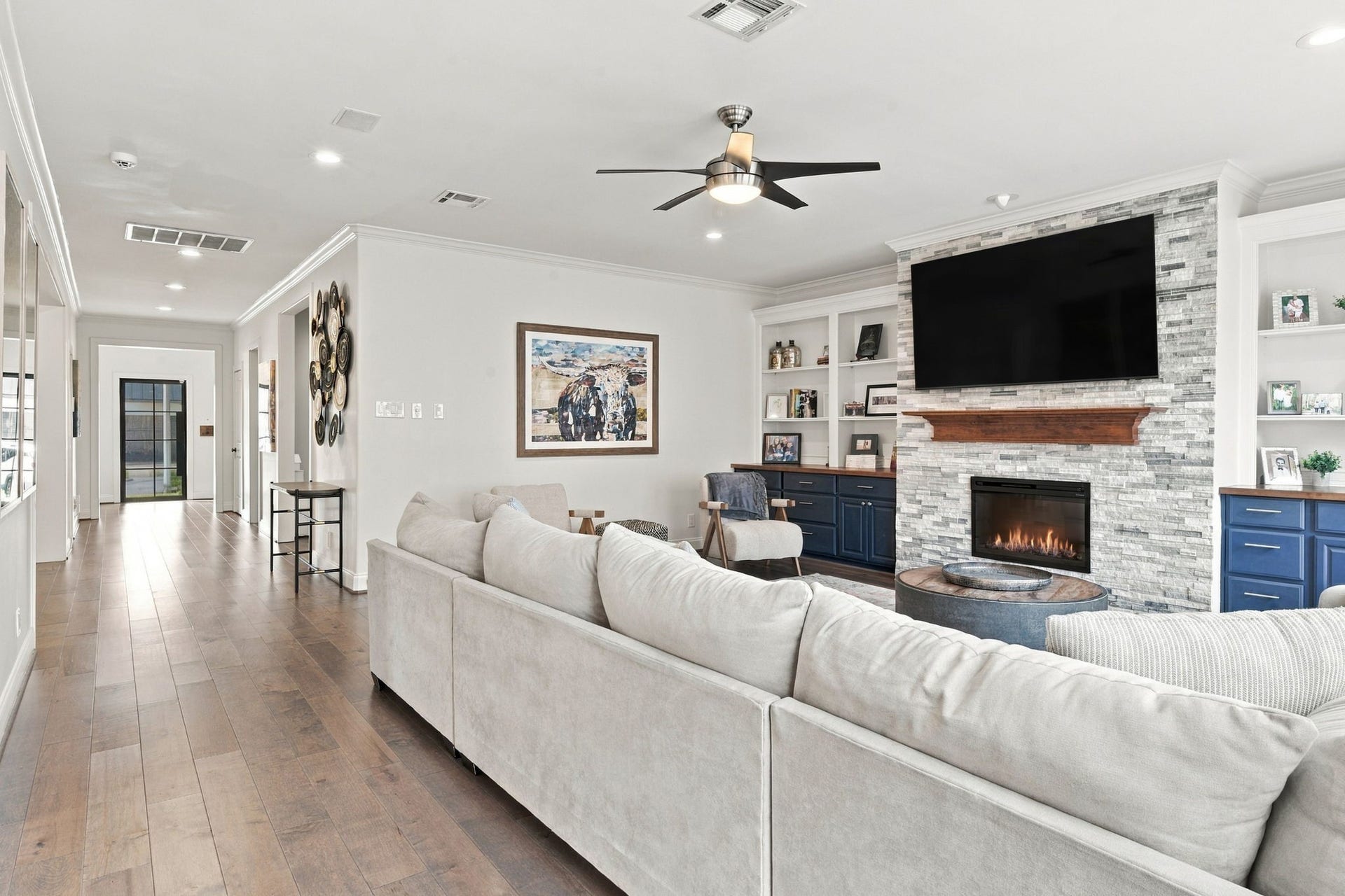 Looking toward the front of the home, this view highlights the living room's connection to the main hallway & surrounding living spaces. Continuous hardwood floors, crown molding & an open, flowing floor plan create a welcoming atmosphere throughout the first floor.