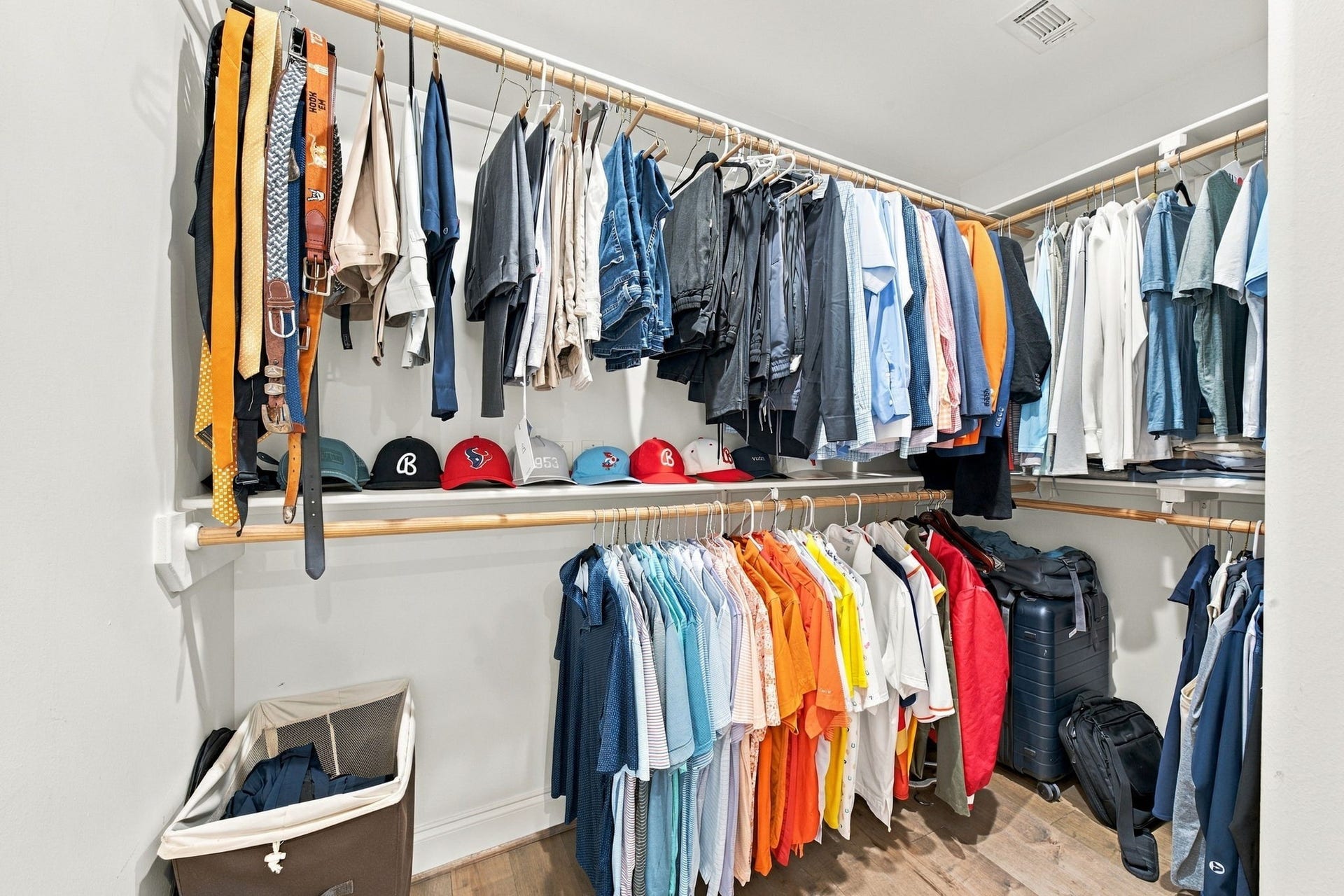 Second primary walk-in closet offers extensive hanging space, multiple clothing rods, open shelving & hardwood floors, providing additional storage & organization.