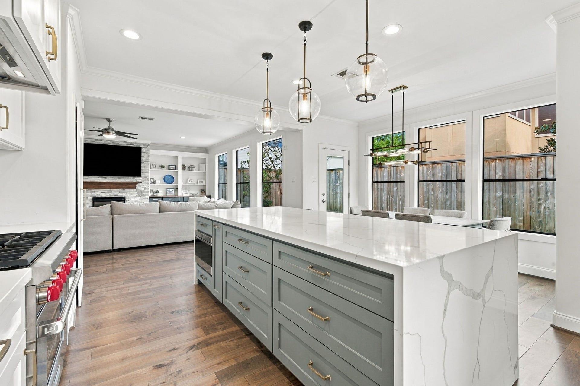Fantastic view highlighting the kitchen's seamless connection to the spacious living room & breakfast area, accented by beautiful glass pendant lighting above the expansive waterfall island.