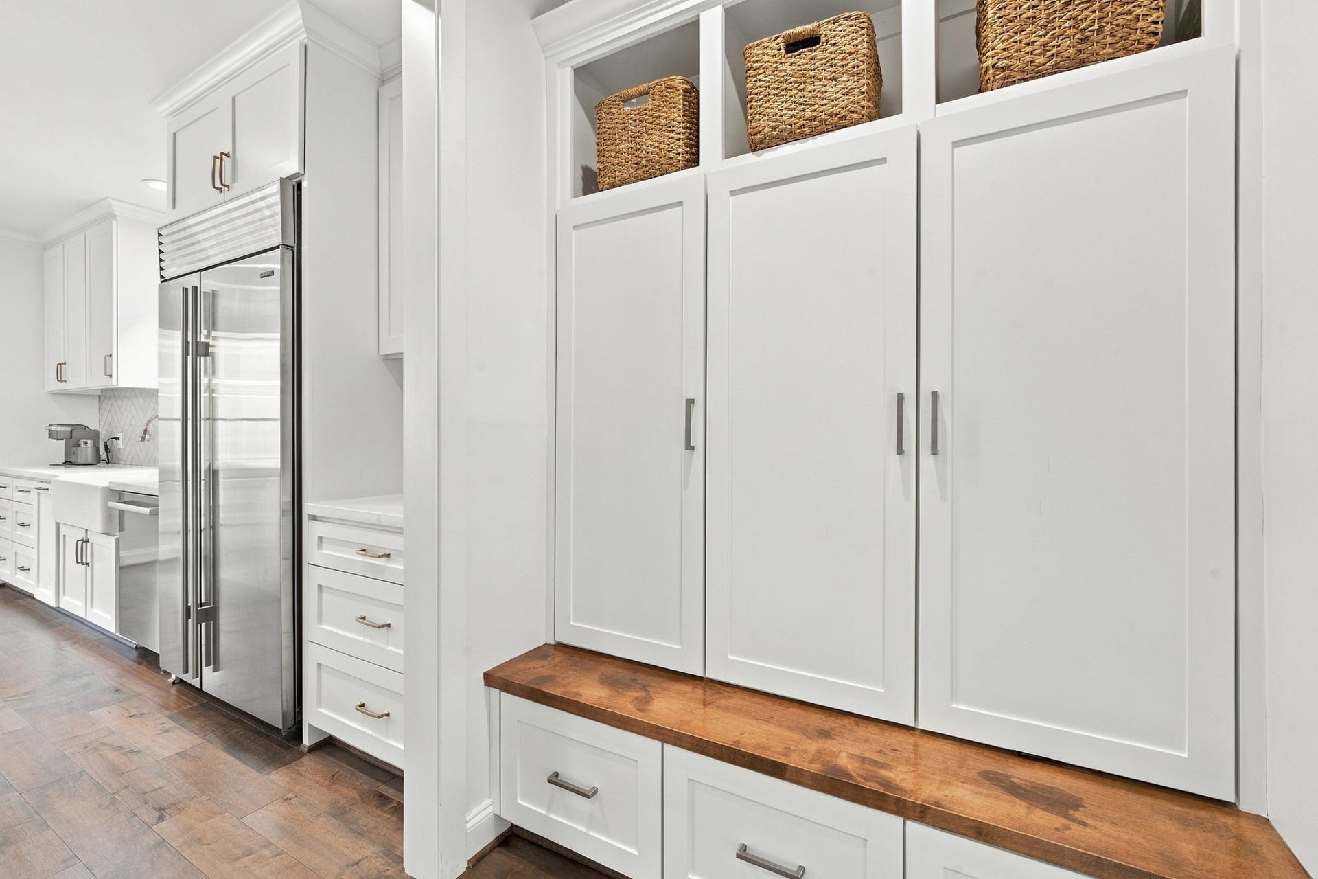 Convenient mudroom located just off the kitchen near the secondary staircase features custom built-in cabinetry, extensive storage, open upper shelving & a beautiful wood bench w/additional drawers below. A thoughtfully designed space for everyday organization & easy access to the kitchen.