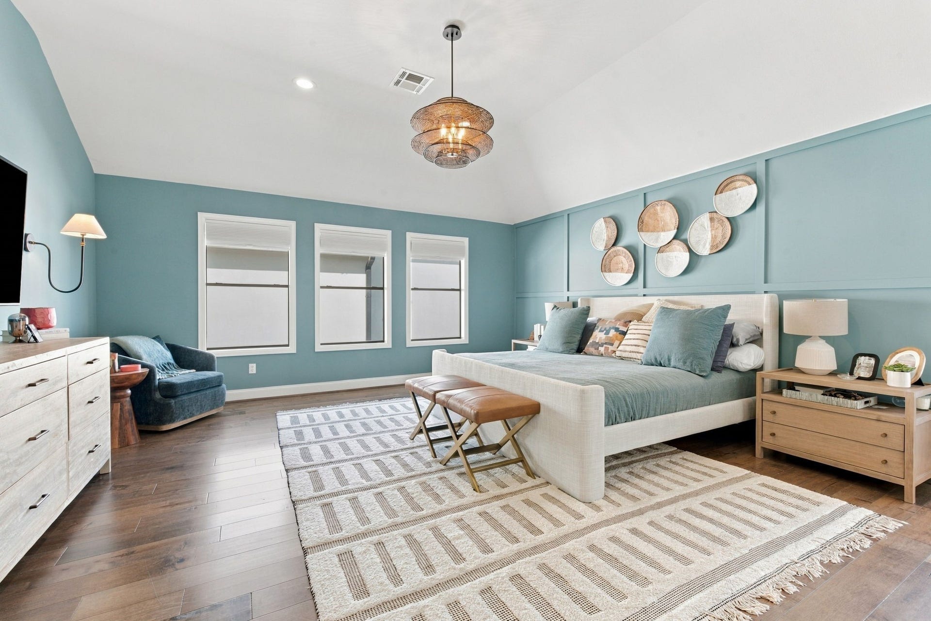 Spacious primary suite showcases beautiful hardwood floors, a striking blue walls w/decorative molding, designer chandelier & recessed lighting. Three windows bring in natural light, creating an inviting and serene retreat w/a comfortable sitting area.