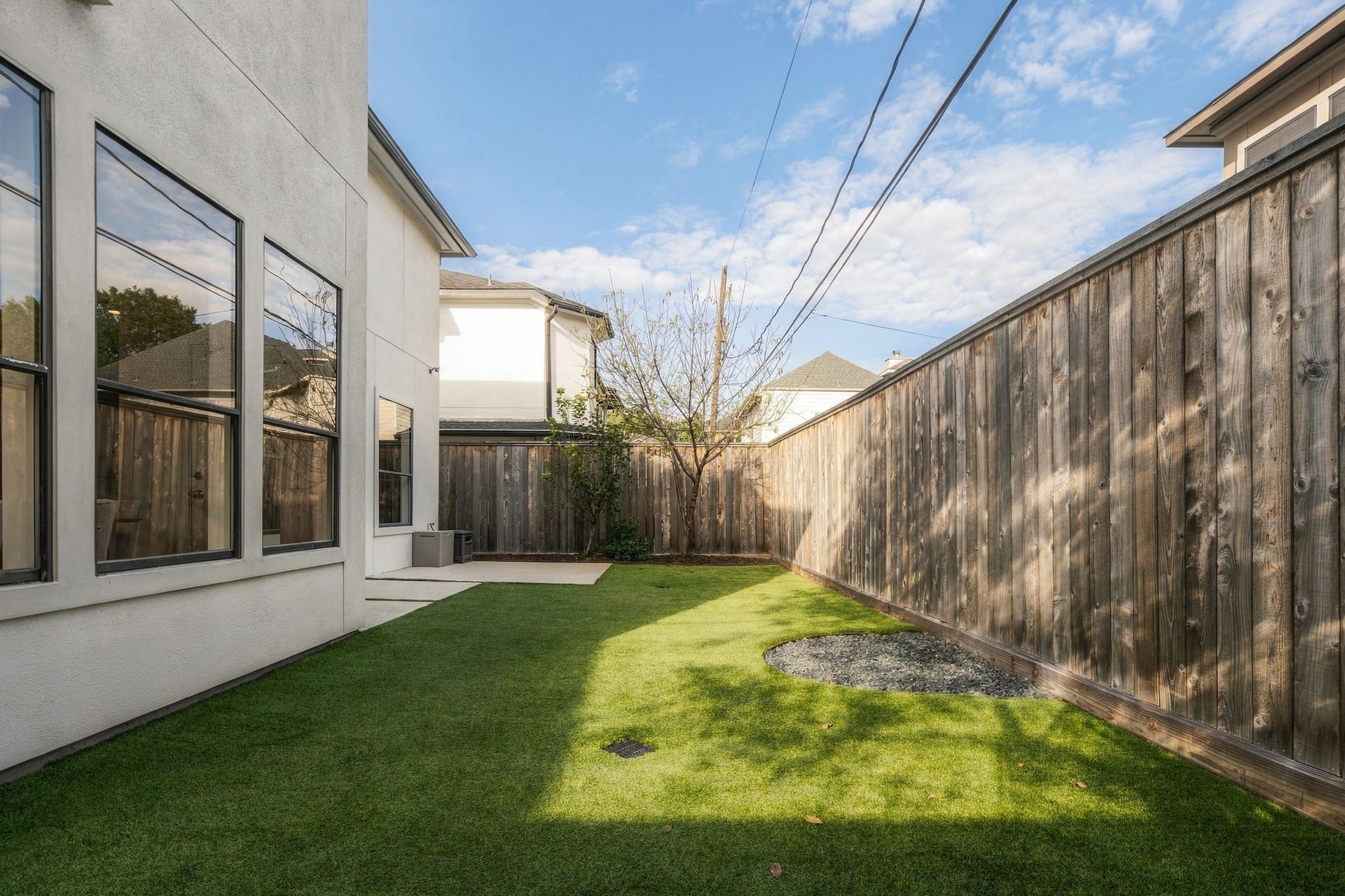 Another perspective of the backyard showcases the expansive turf lawn, mature trees & wood fencing. This inviting outdoor space offers room for recreation, pets & everyday enjoyment, w/easy access to the patio & home.