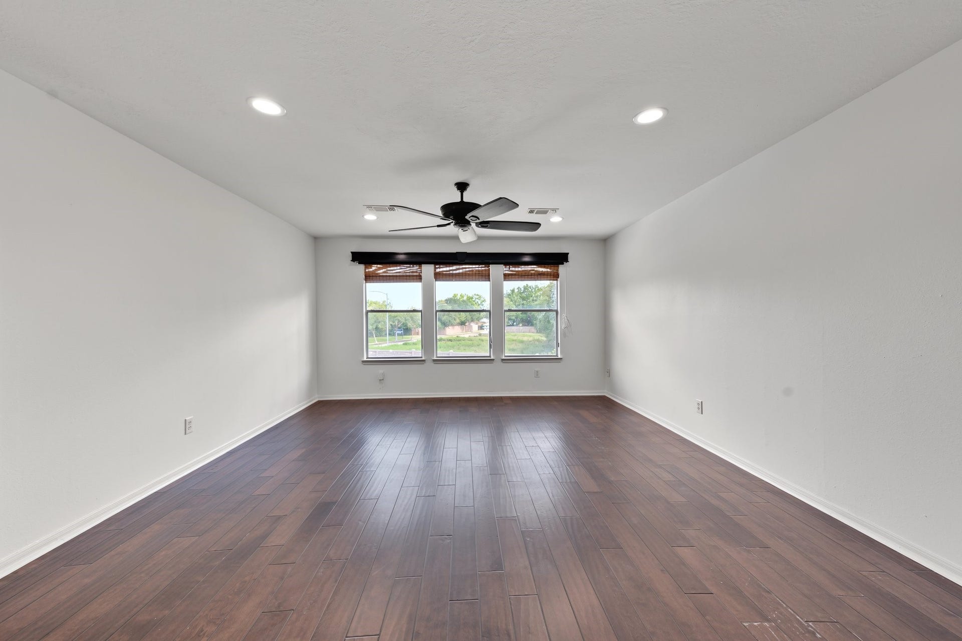 Large game / media room with rich hardwood flooring, a modern ceiling fan, and natural light streaming through large windows. Ready for making memories...