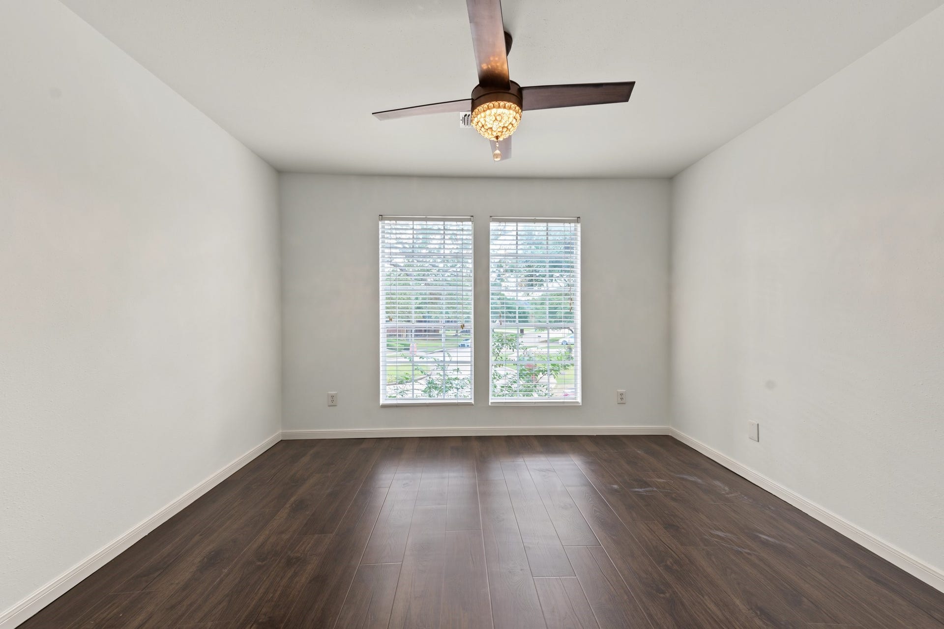 Bright and airy room featuring large windows, sleek hardwood floors, and a stylish ceiling fan. All it needs is your family...