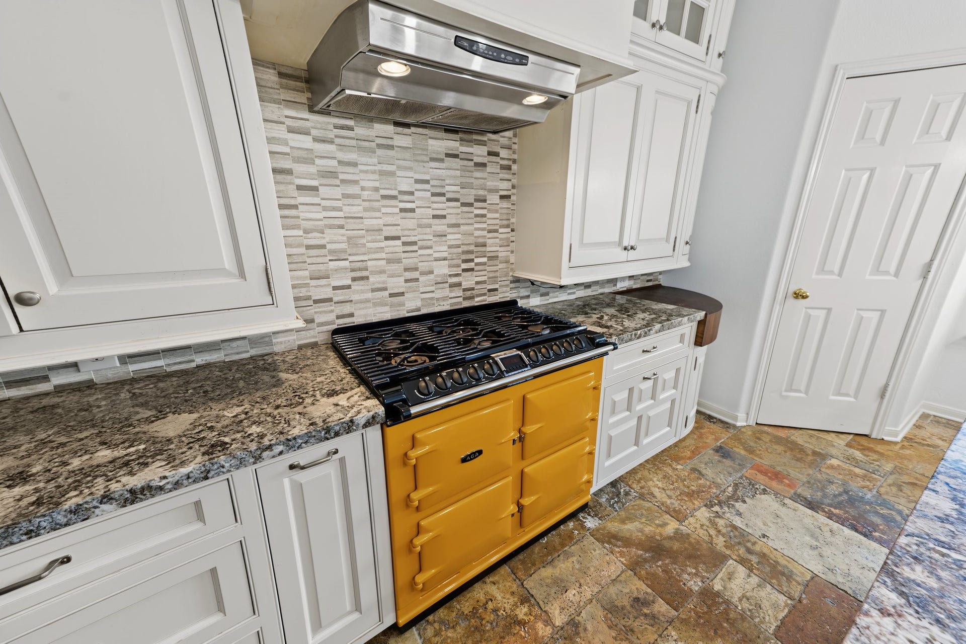 Charming kitchen featuring a vibrant yellow range, sleek granite countertops, and elegant white cabinetry, complemented by a stylish tile backsplash. The AGA range, is a high end stove. AGA is a well known British brand, famous for it's distinctive, heavy duty cookers and traditional country kitchens.