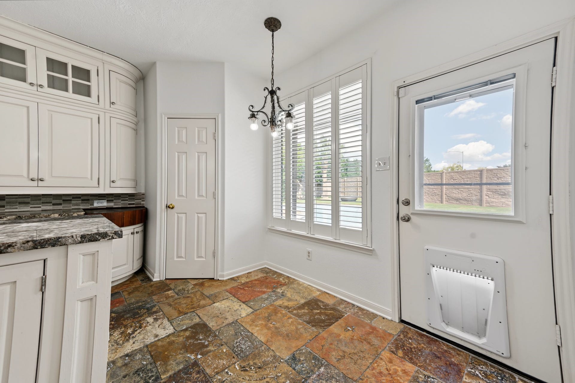 Bright and inviting kitchen space featuring elegant tile flooring, granite countertops, and natural light from large windows and a glass door. Already equipped with a doggie door for your fur babies easy access to the back yard.