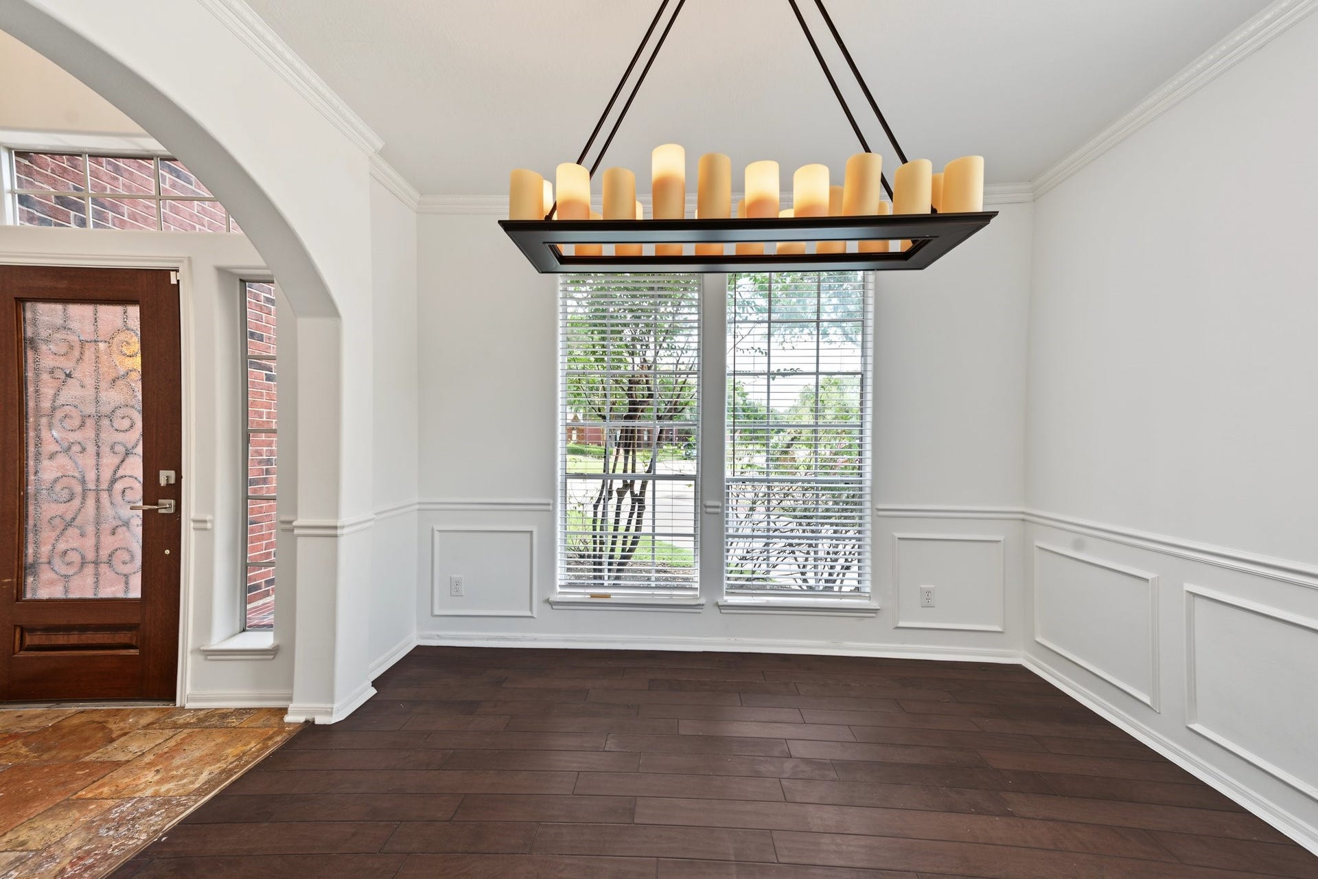The dining room features a stylish chandelier, rich wood flooring with intricate glass detailing, complemented by large windows for ample natural light. Would also make a great home office.