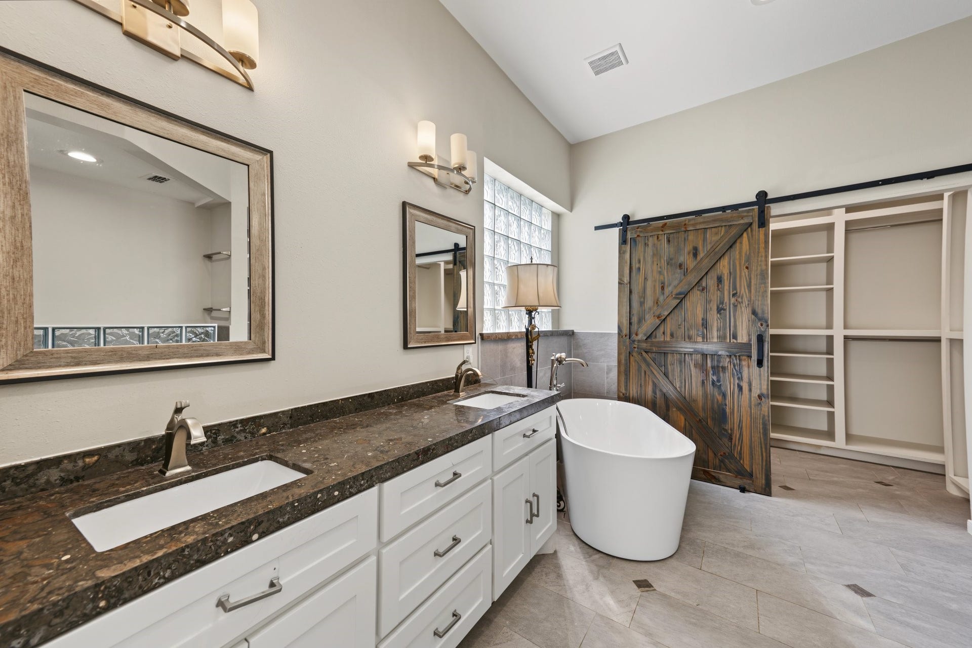 Spa-like...Stunning and enormous primary en-suite bathroom featuring a luxurious freestanding tub, dual sinks with granite countertops, and a rustic sliding barn door leading to the highly functional built-in closet.
