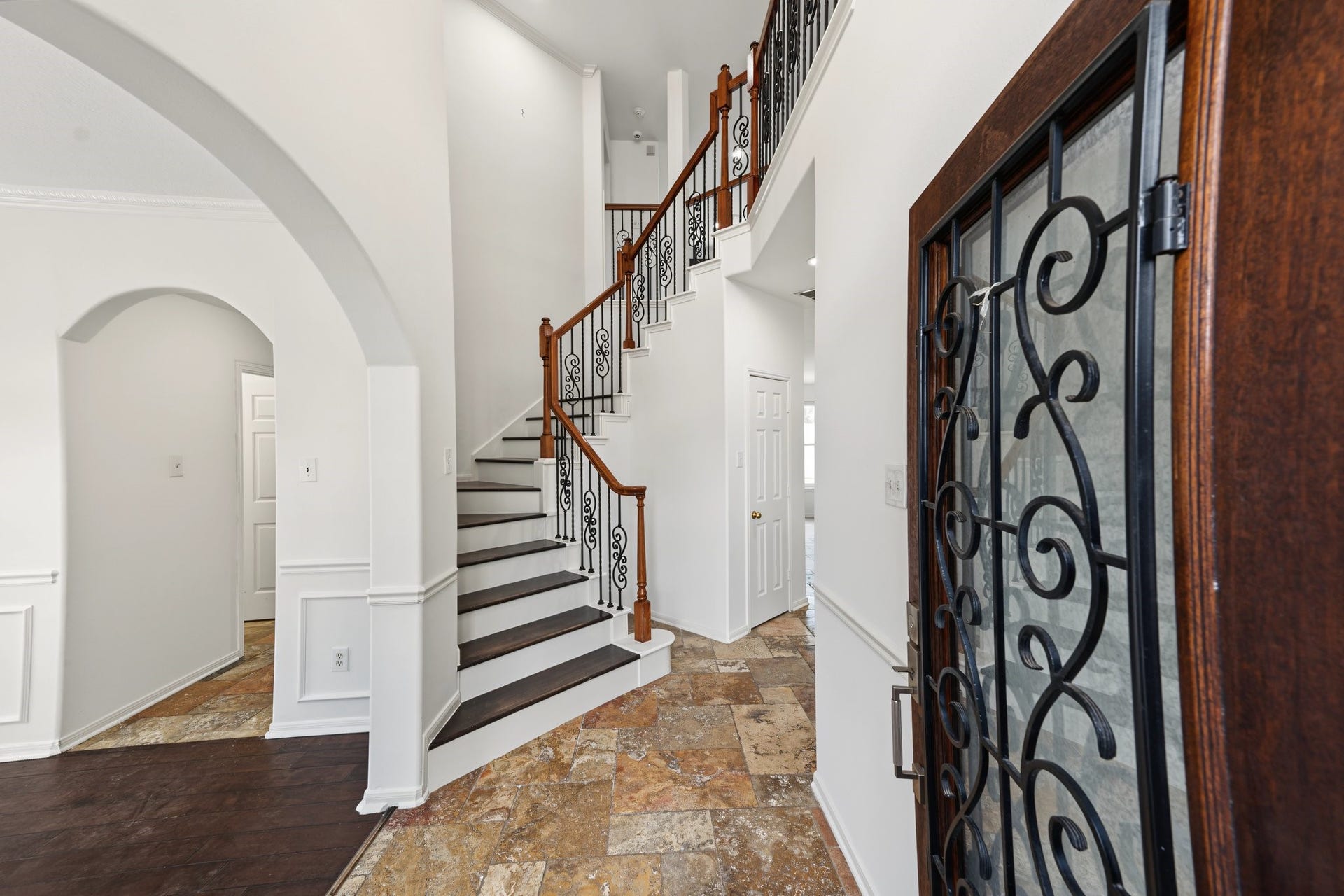Entryway featuring a wrap-around staircase with wrought iron railings, arched doorways, and rich flooring that seamlessly blends tile and wood accents.