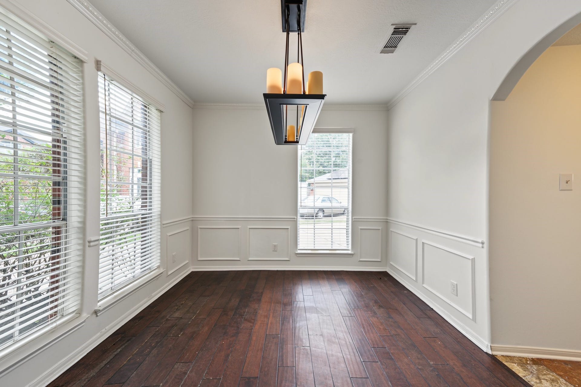 This dining room features rich hardwood floors, chair railing and wainscoting with abundant natural light from large windows, and a stylish modern chandelier.