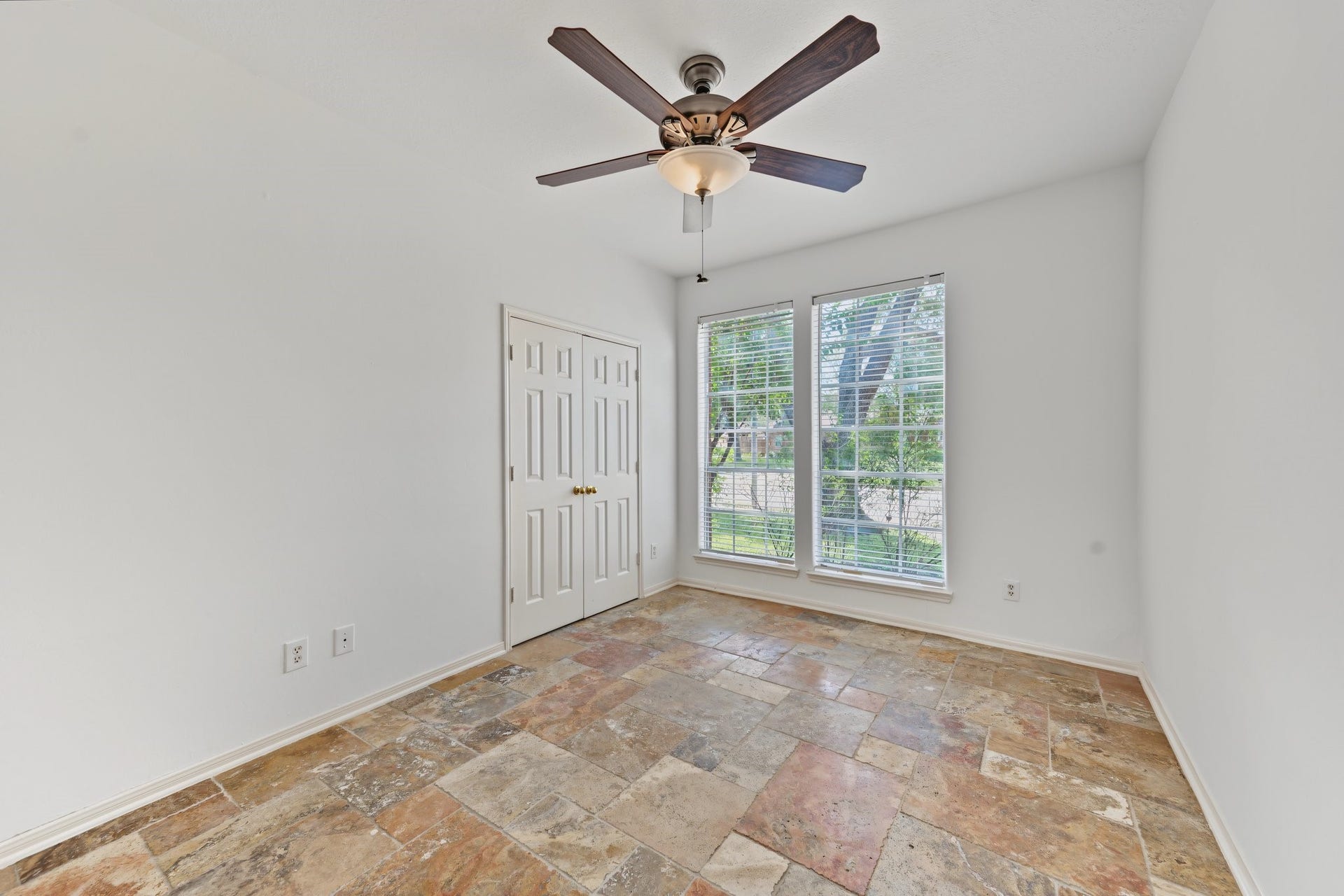 The second downstairs bedroom is bright, with large windows, tile flooring, and a ceiling fan, offering a comfortable and inviting space.