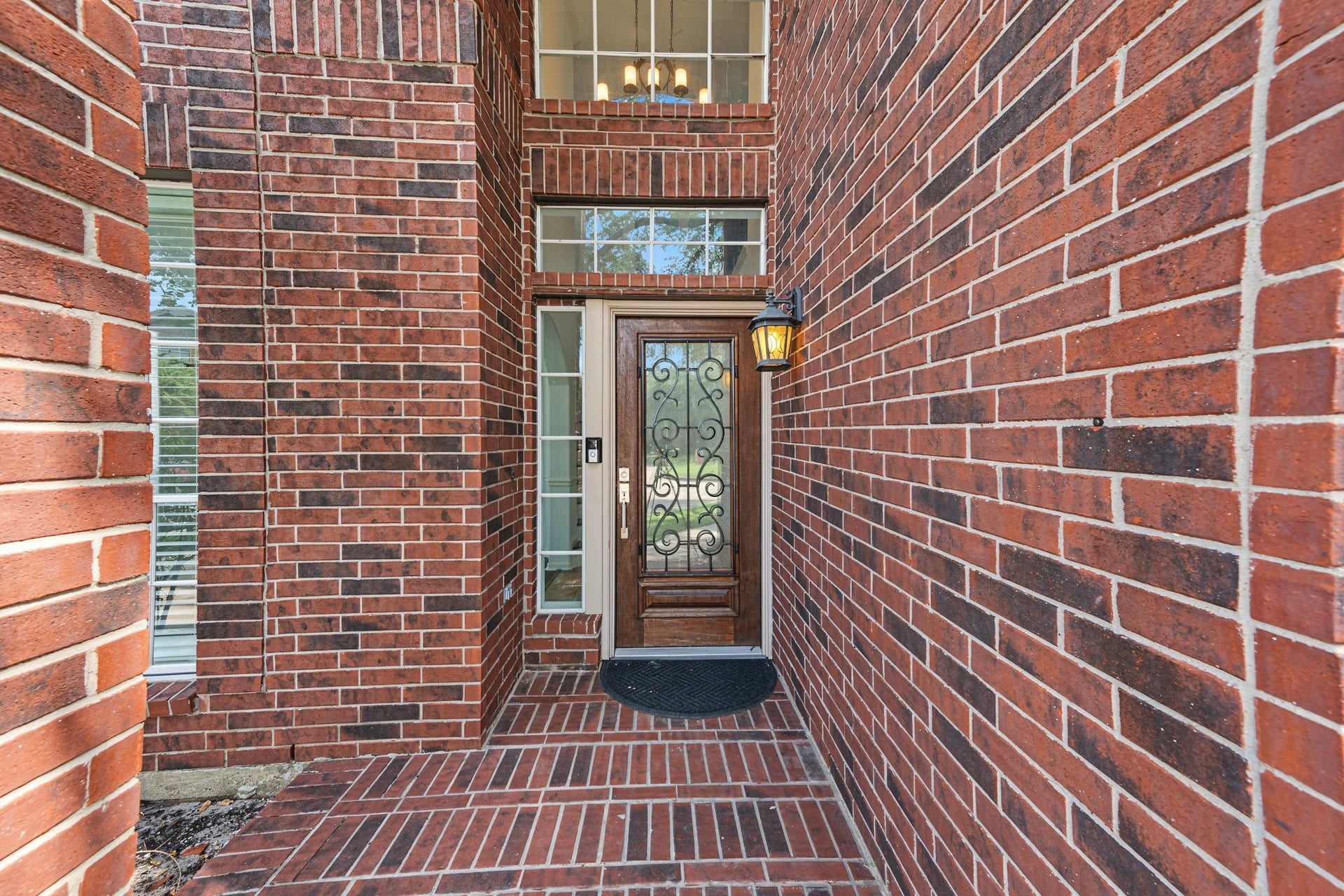 Durable brick entryway featuring a decorative glass door and charming lantern lighting, provides a warm welcome to your new home.
