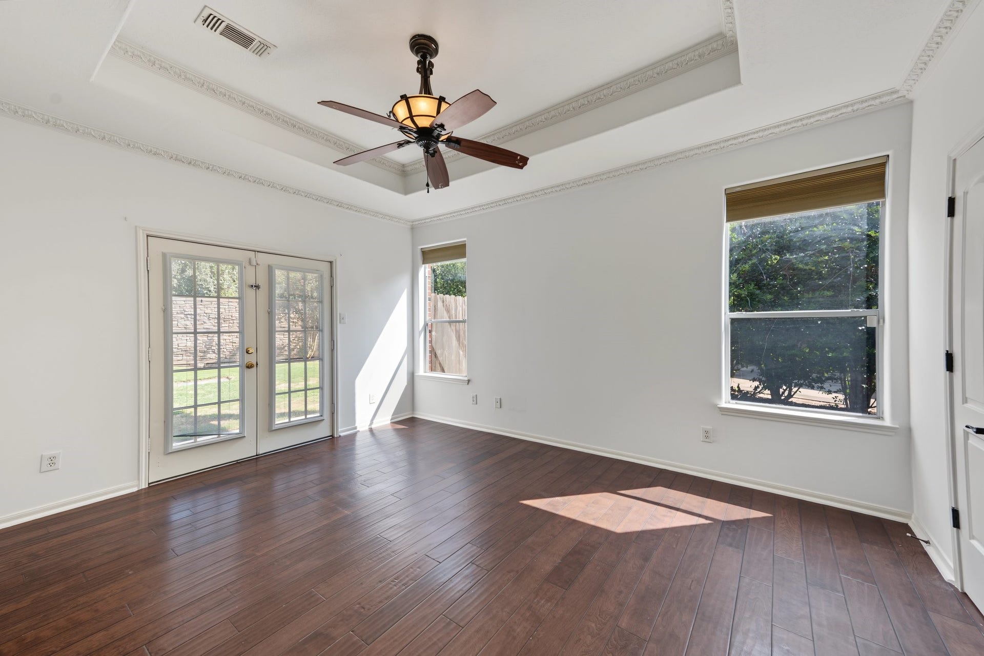 Here it is! The primary suite is bright and inviting featuring elegant wooden flooring, crown molding, a ceiling fan, and French doors leading to the large backyard and pool / hot tub. An en-suite bathroom is adjacent providing privacy.
