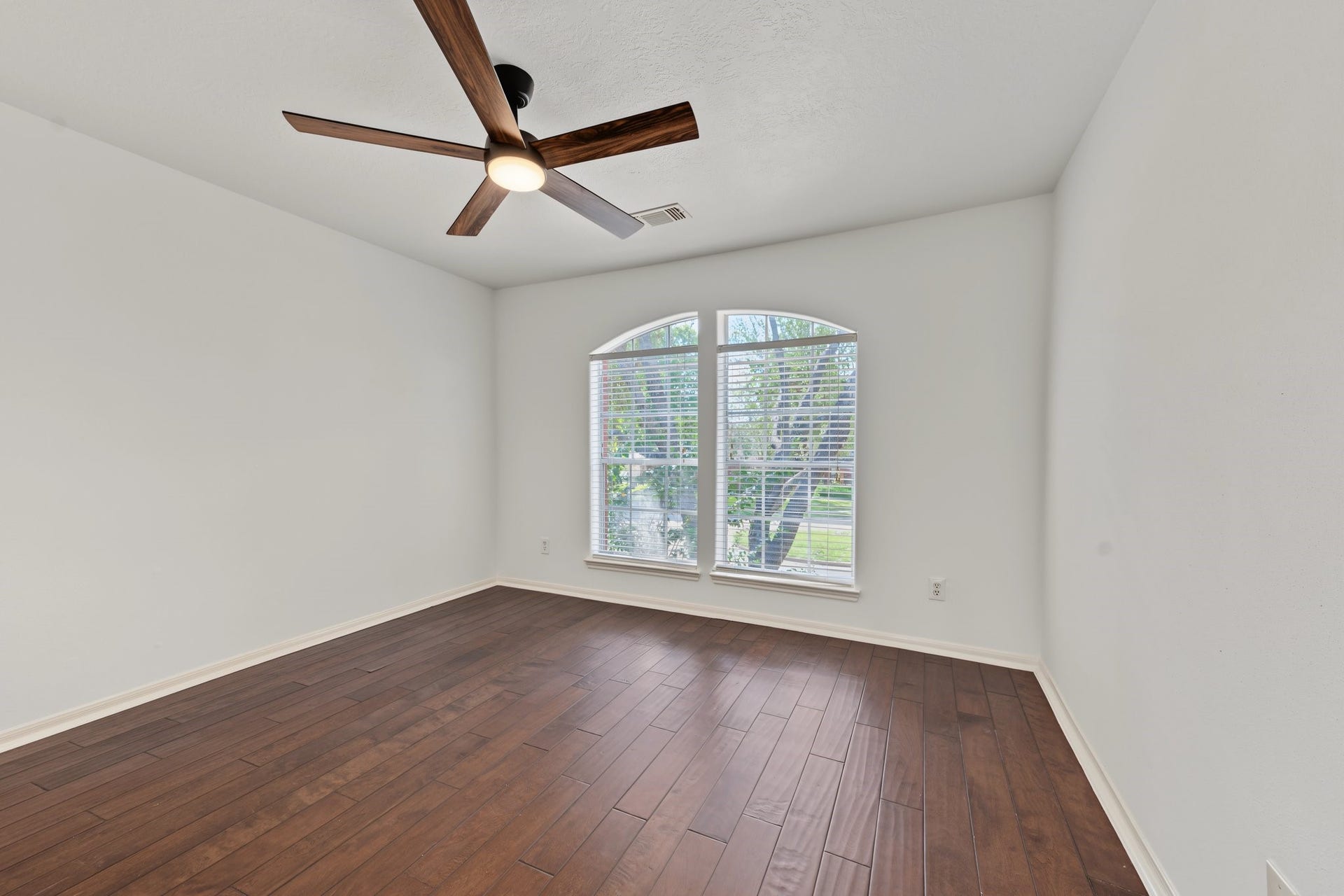 Secondary bedroom with hardwood floors, a stylish ceiling fan, and a large arched window offering abundant natural light.