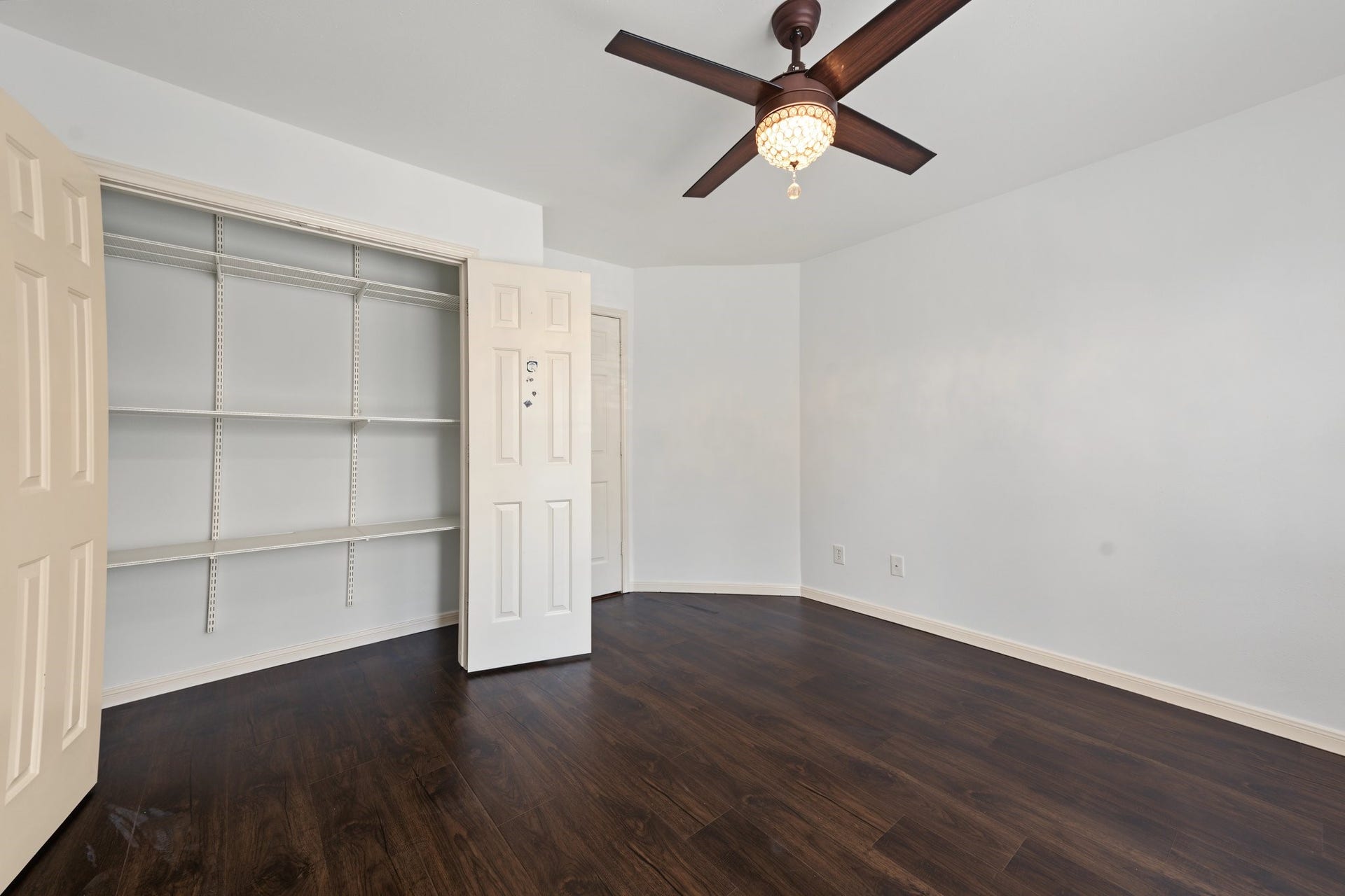 Secondary bedroom with rich dark wood flooring, a modern ceiling fan, and ample closet space with built-in shelving. Great space!