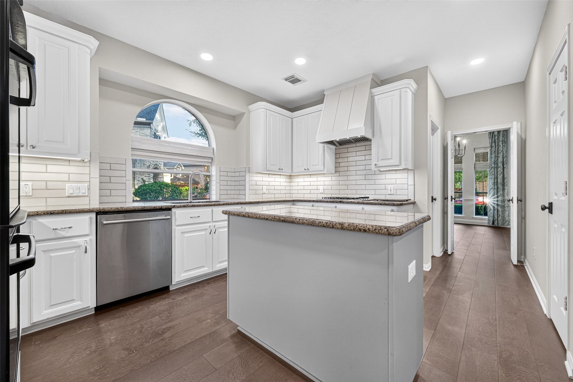 7707 Stone Arbor Drive, Sugar Land, TX 77479 A KITCHEN DESIGNED FOR EVERYDAY LIVING! Bright white cabinetry, granite countertops, a subway tile backsplash & beautiful wood flooring create a welcoming space for preparing meals & gathering throughout the day. The center island provides additional workspace, while the arched window over the sink adds architectural character. Notice the recessed lighting, decorative vent hood & convenient access to the Formal Dining Room.