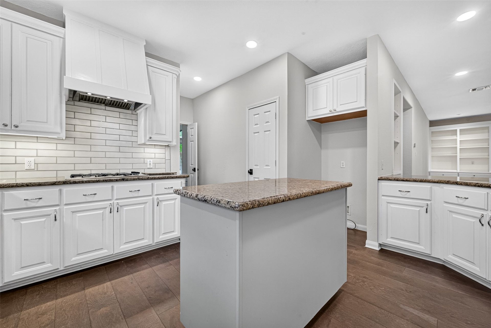 7707 Stone Arbor Drive, Sugar Land, TX 77479 THERE'S MORE TO THIS KITCHEN THAN MEETS THE EYE! This view highlights the center island, gas cooktop & additional built-in cabinetry beyond the main cooking area. Open shelving and countertop space provide opportunities for organizing everyday essentials, displaying favorite pieces or creating a convenient beverage station. The nearby pantry adds another practical storage feature.
