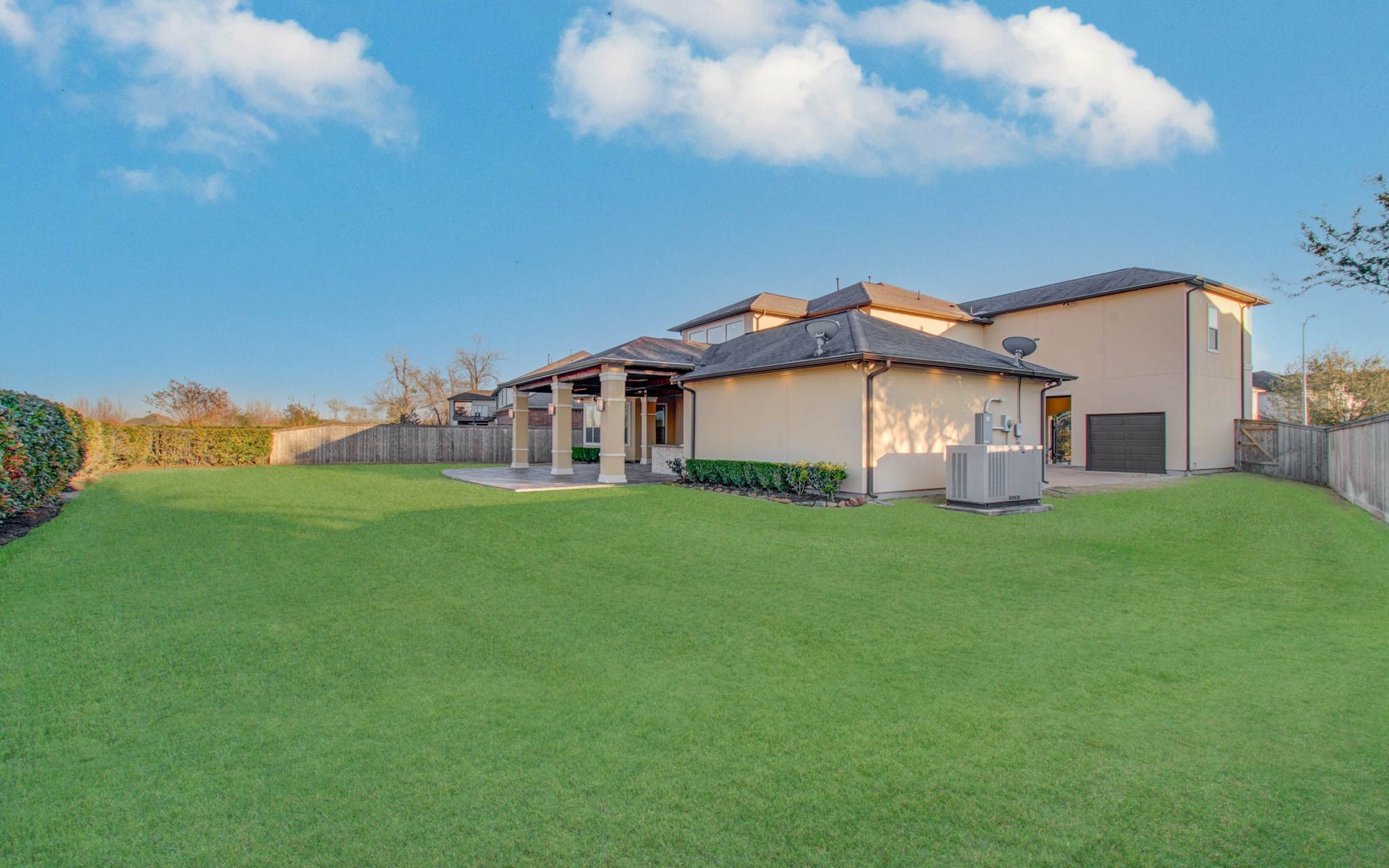 Spacious backyard with well-maintained grass, featuring a covered patio area. The home has a modern exterior with a two-story design, surrounded by a wooden fence for privacy. Perfect for outdoor activities and entertaining.