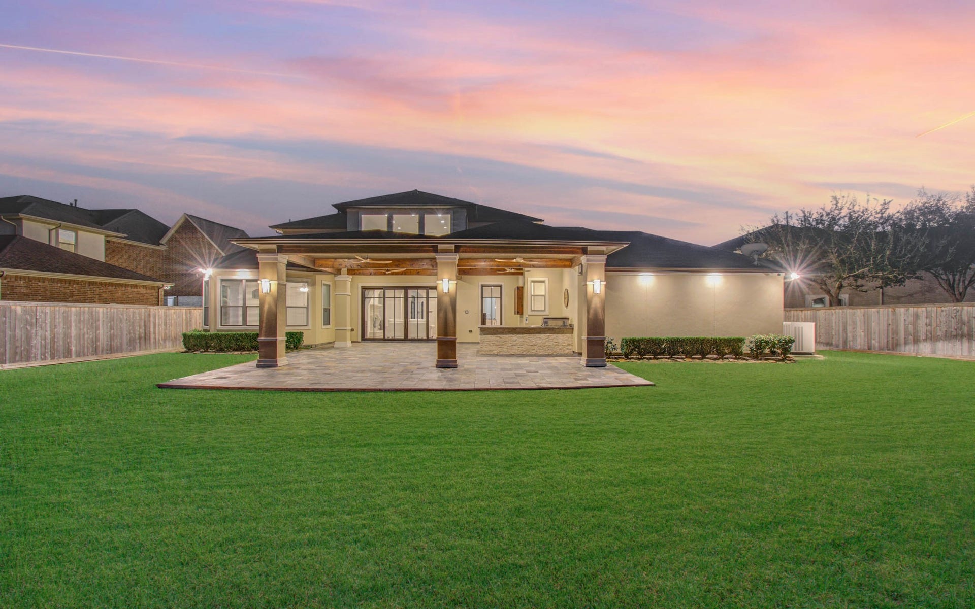 This photo showcases a spacious backyard with lush green grass and a large covered patio featuring elegant columns and lighting. It's an ideal space for outdoor entertaining, set against a beautiful sunset sky.