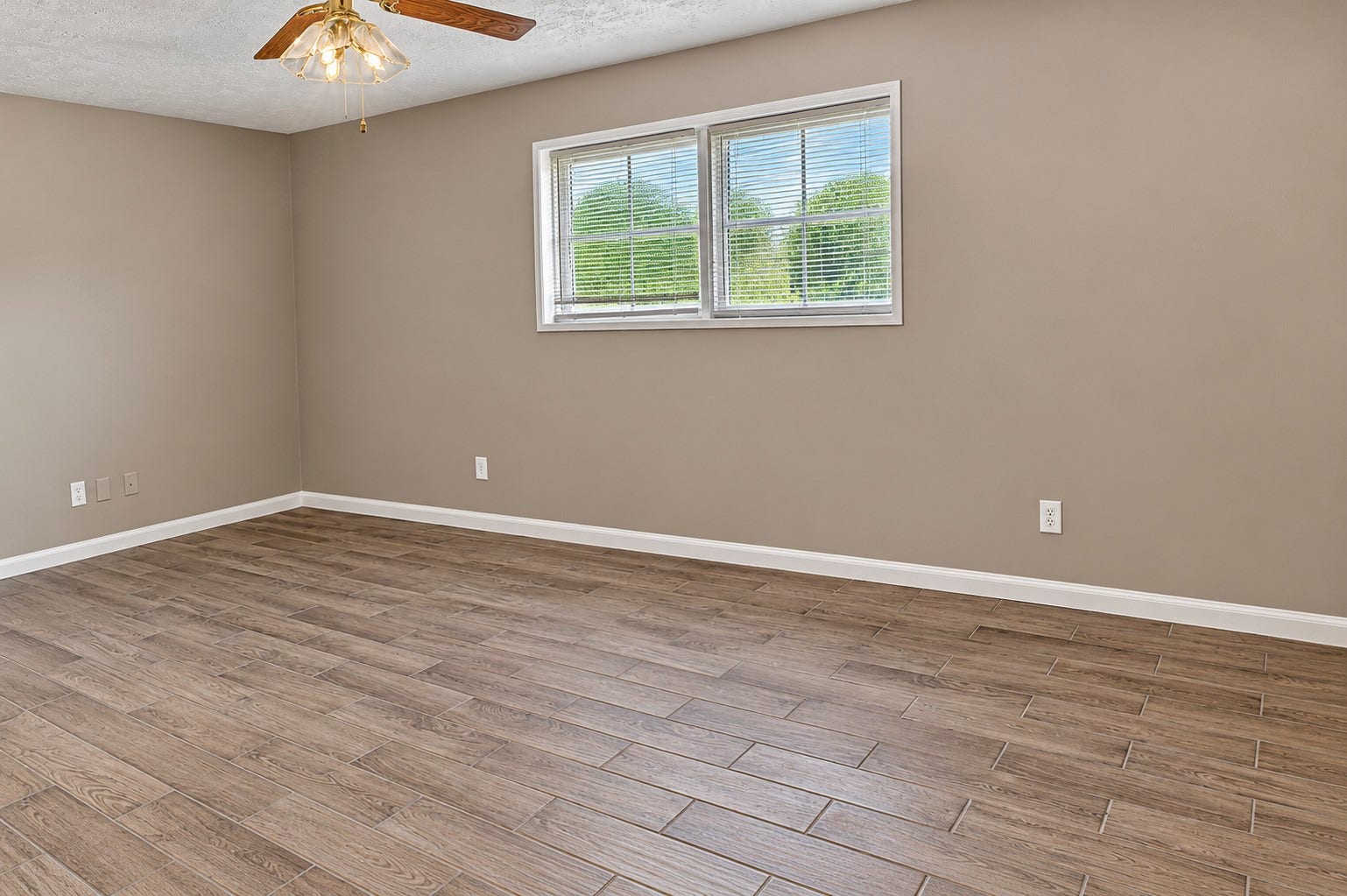 Spacious bedroom with wood-look tile flooring, neutral walls, and a ceiling fan, perfect for versatile living arrangements.