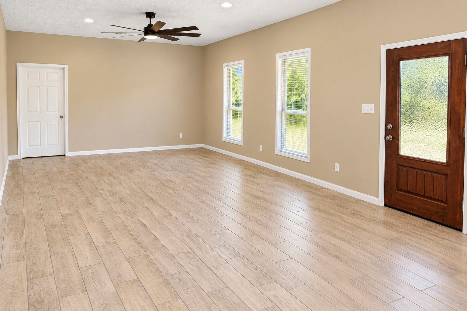 Spacious living area with elegant wood-style tile flooring, abundant natural light from large windows, and a stylish ceiling fan.