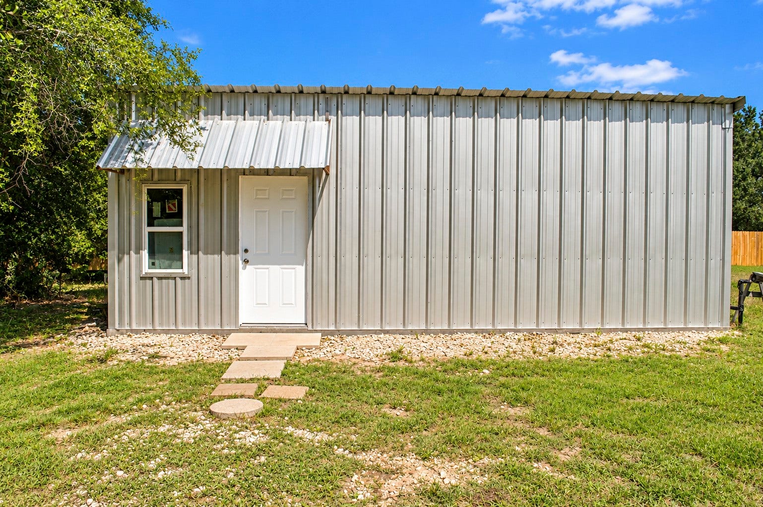 Charming metal-clad tiny multipurpose building with a welcoming entrance, nestled in a serene green setting.