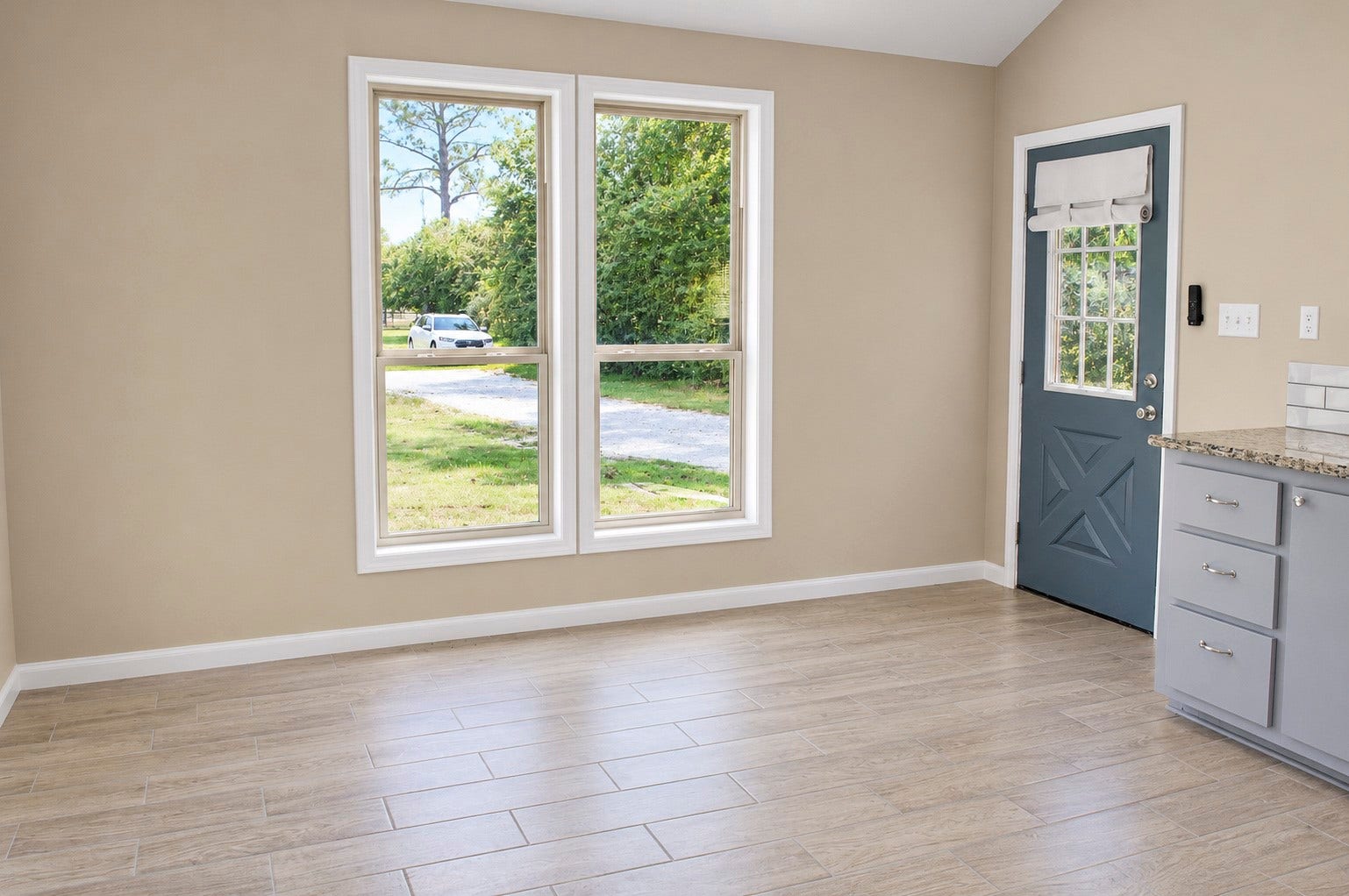 Bright and inviting breakfast space with large windows, wood-look tile flooring, and a charming blue door leading to the outside.