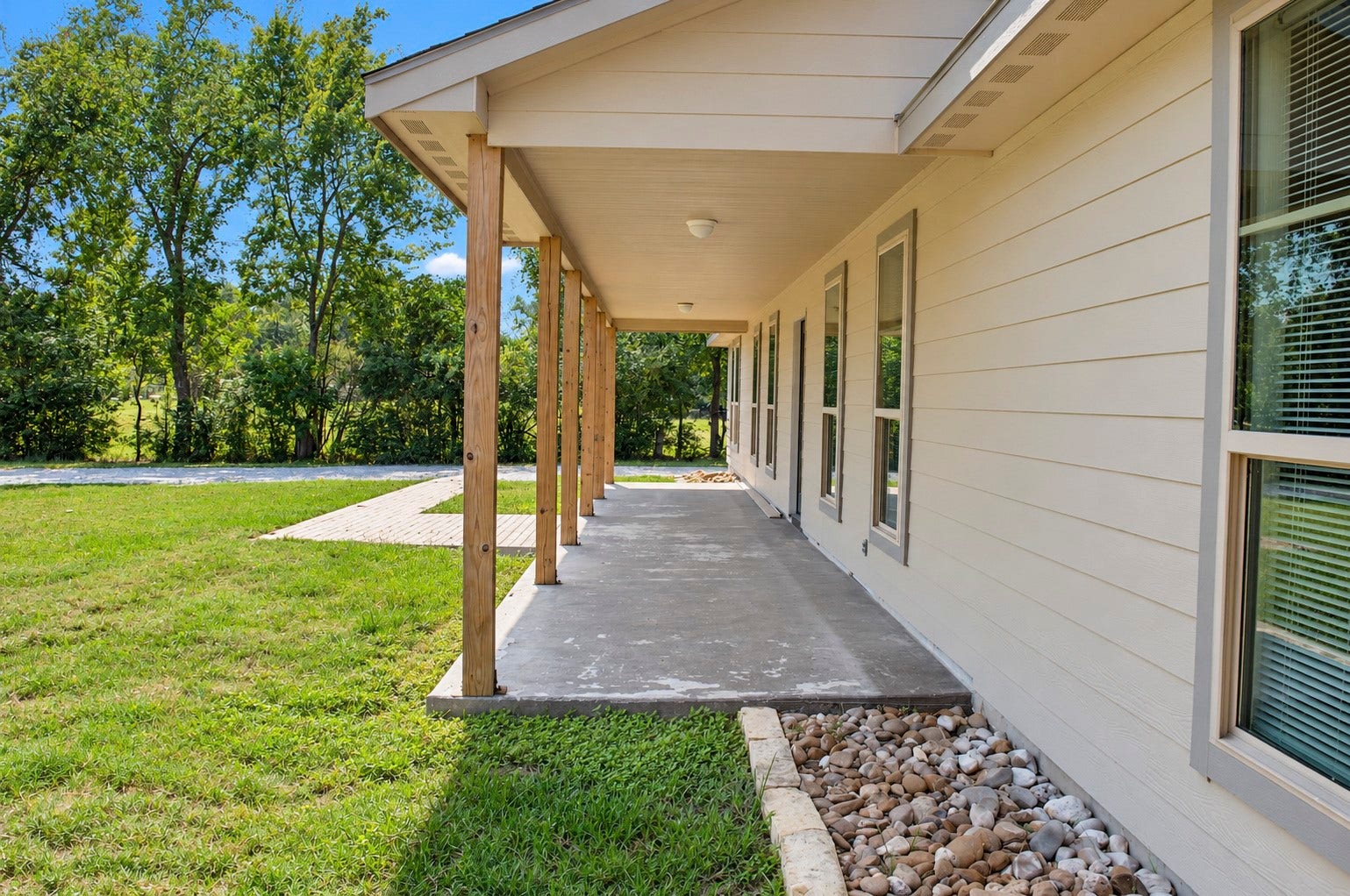 Charming covered porch with a concrete walkway and natural stone landscaping and a spacious yard.