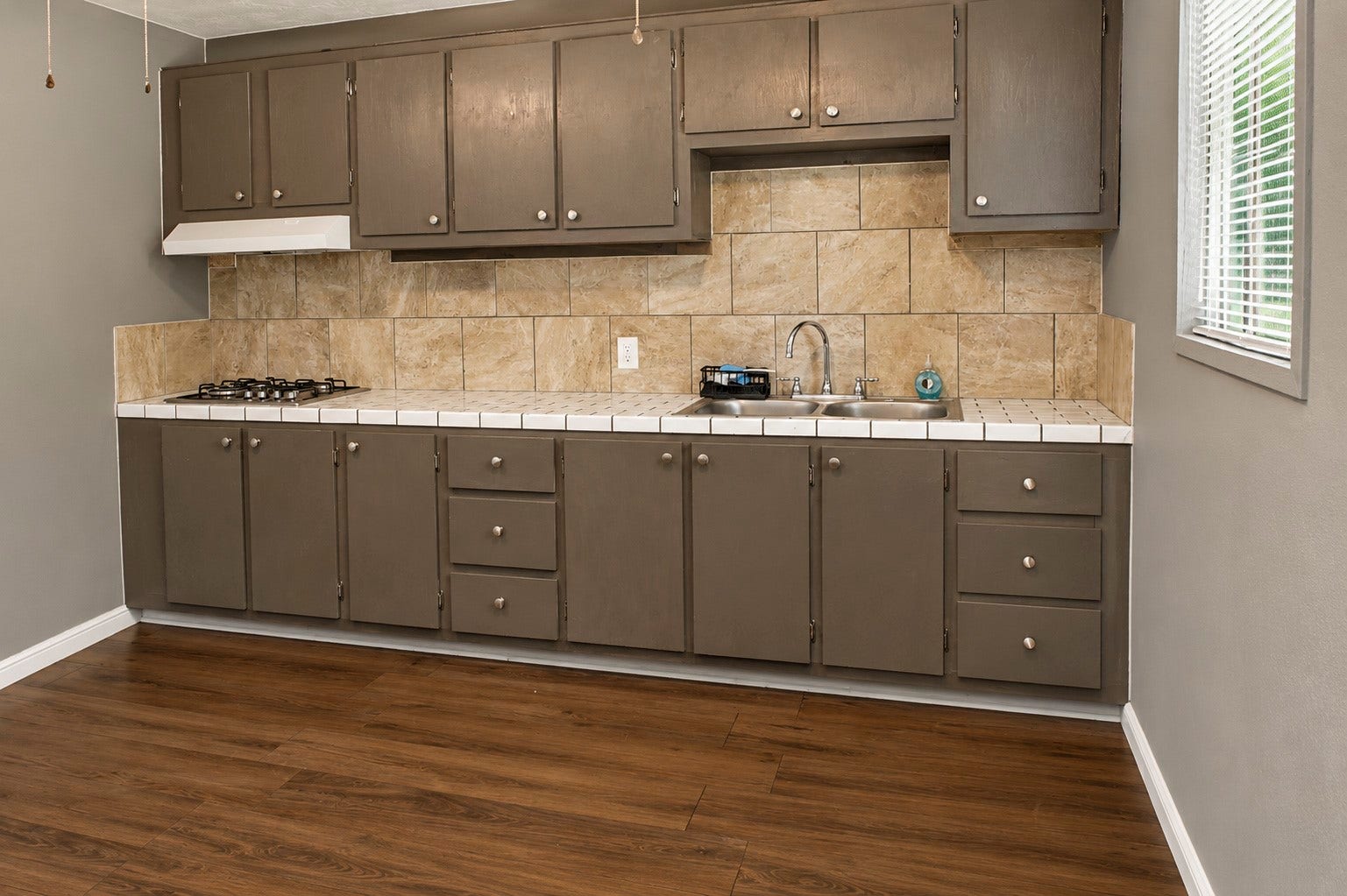 Quarter's kitchen with rustic brown cabinetry, sleek tile backsplash.