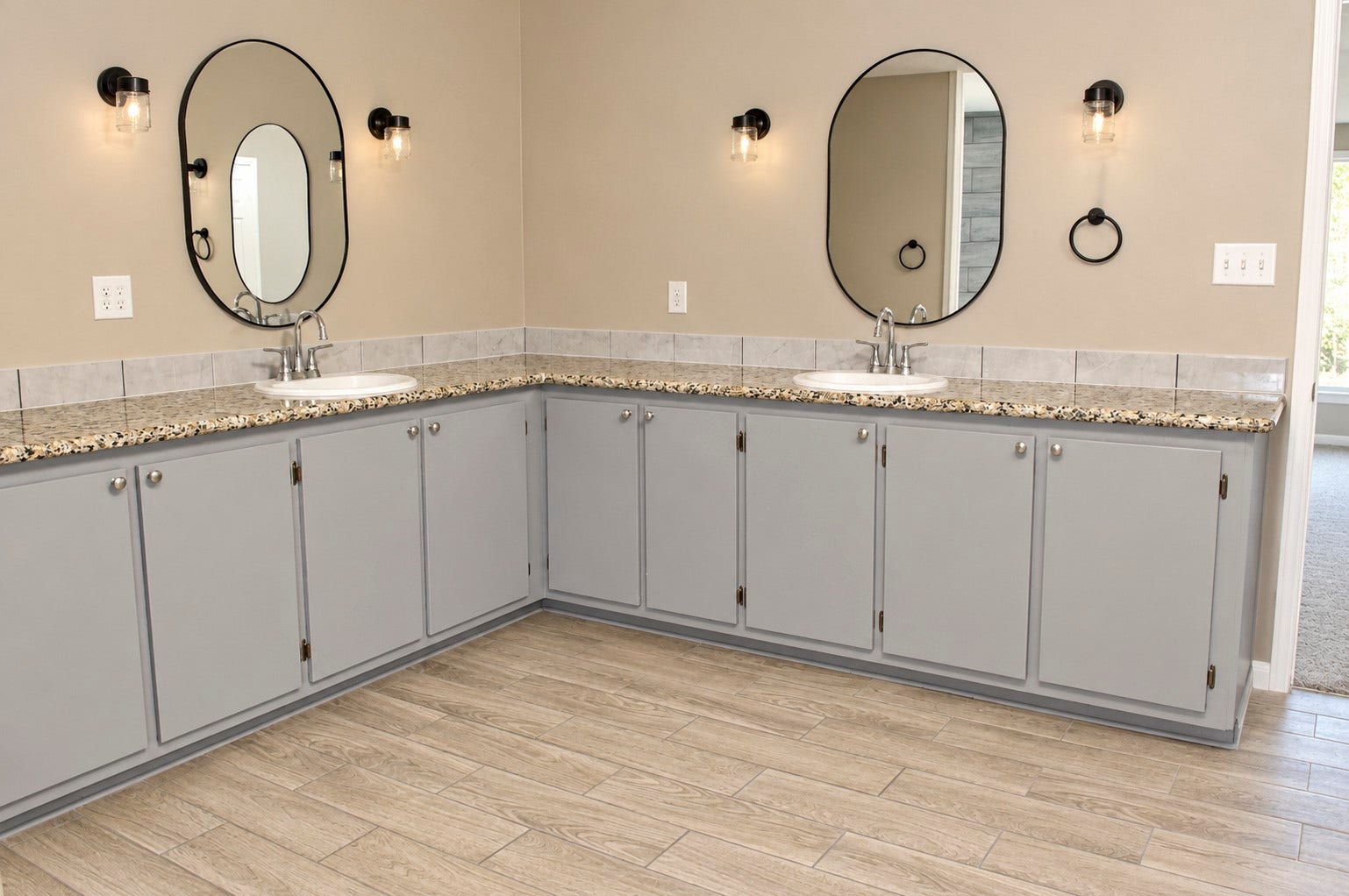 Spacious Primary bathroom featuring dual sinks with elegant granite countertops, sleek gray cabinetry, and stylish round mirrors enhanced by modern lighting.