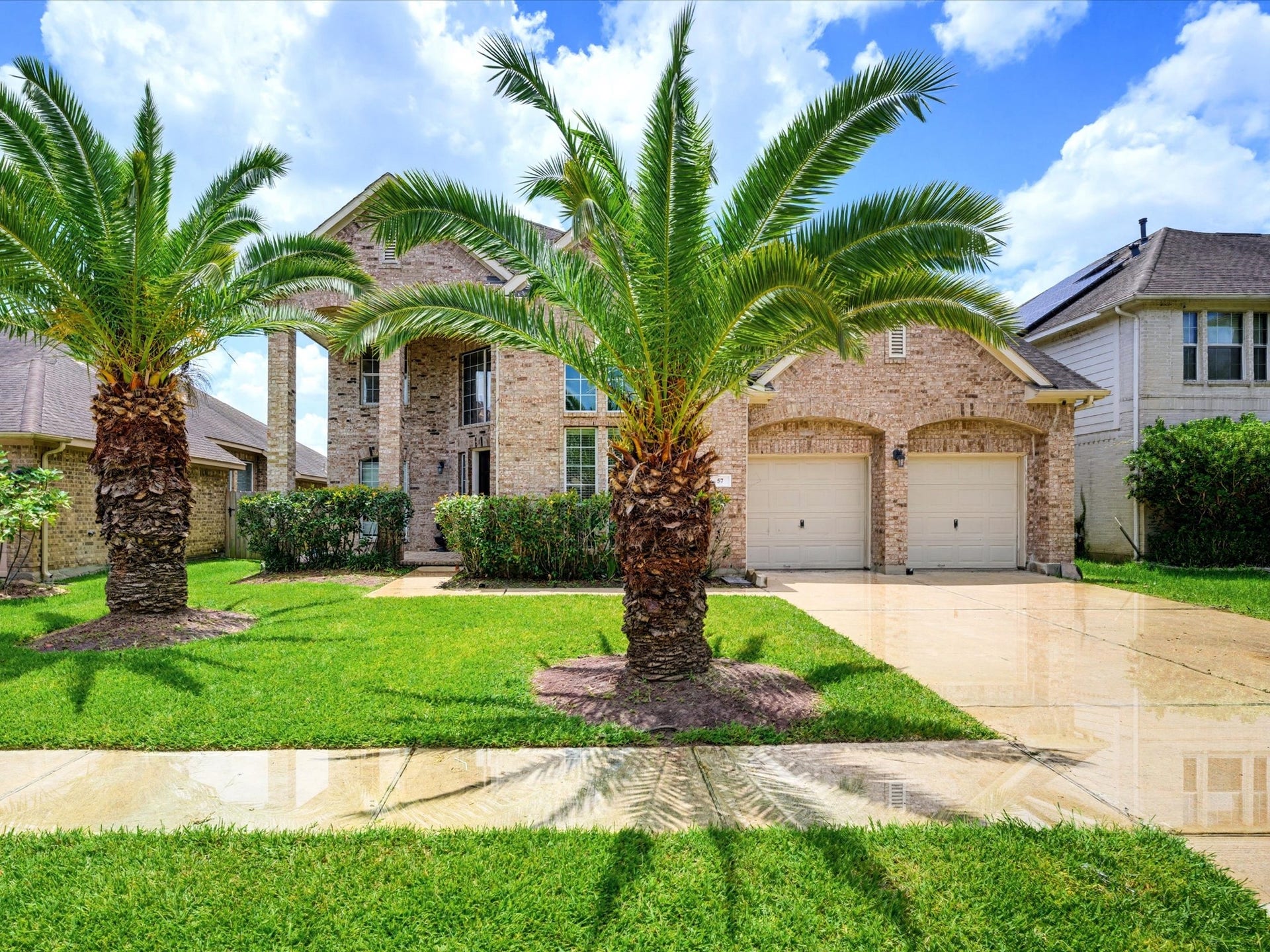 57 Terra Bella Dr, Manvel, TX 77578 Beautiful two-story brick home with mature palm trees, a dramatic covered entry and an attached two-car garage.