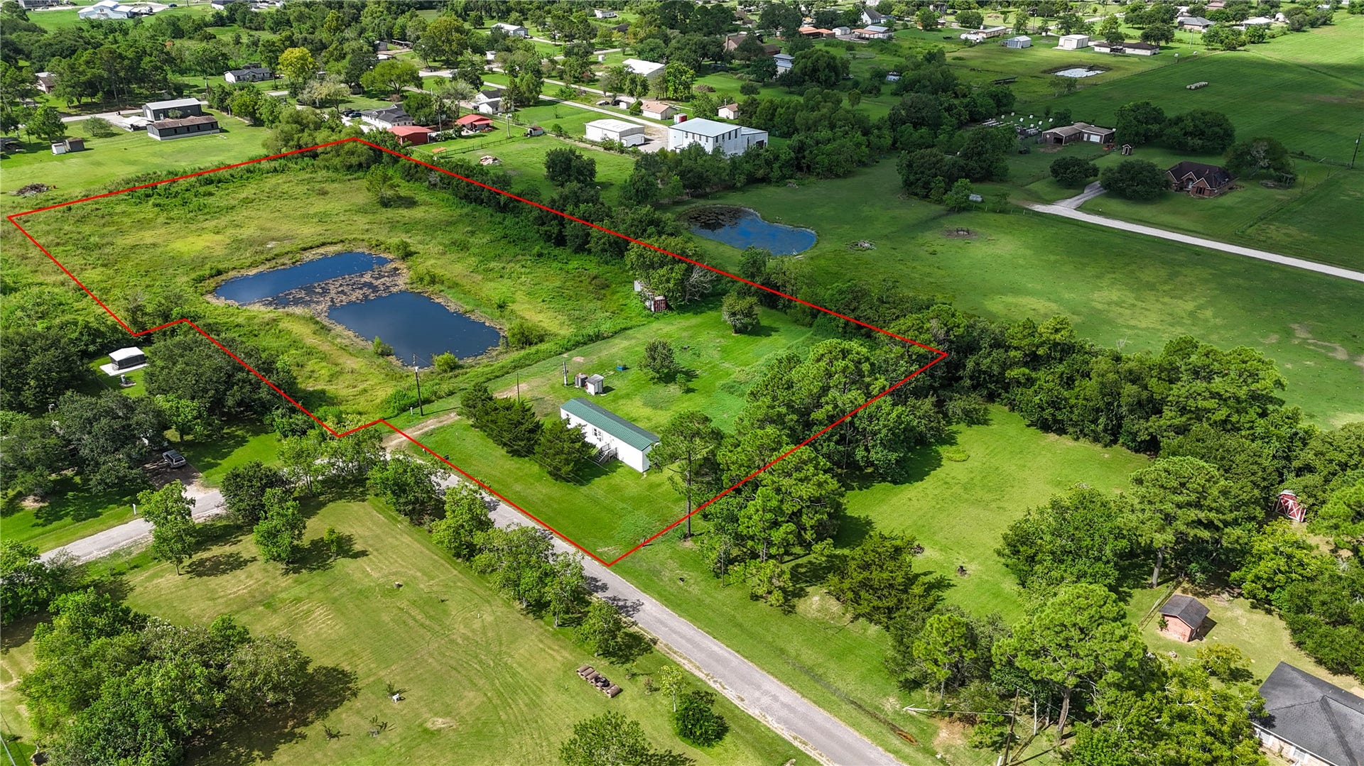 Expansive green property with a delineated boundary, featuring a serene pond and surrounded by lush trees, offering ample space and tranquility.