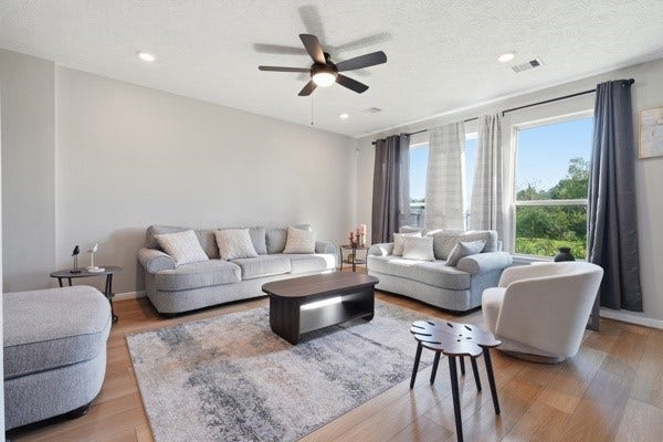 15334 Silver Breeze Lane, Houston, TX 77044 Spacious and bright living room featuring modern gray sofas, sleek hardwood floors, and large windows offering abundant natural light.