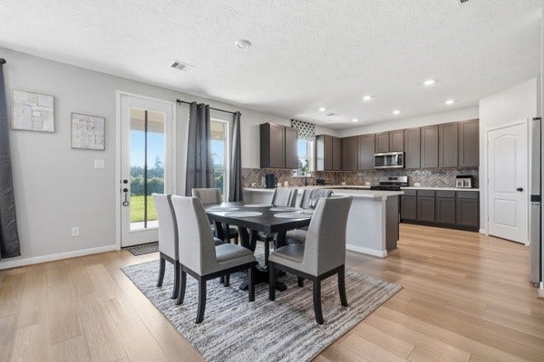 15334 Silver Breeze Lane, Houston, TX 77044 Bright and inviting open-concept dining and kitchen area featuring sleek cabinetry, modern appliances, and elegant wood flooring, with large windows offering plenty of natural light and a view of the outdoors.