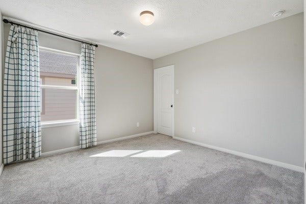 15334 Silver Breeze Lane, Houston, TX 77044 Bright and airy bedroom with soft carpeting and ample natural light, featuring a large window with stylish curtains and a classic closet door.