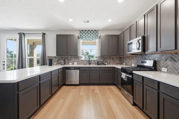 15334 Silver Breeze Lane, Houston, TX 77044 Spacious kitchen with sleek dark cabinetry, modern stainless steel appliances, and elegant herringbone backsplash, complemented by abundant natural light and warm wood flooring.