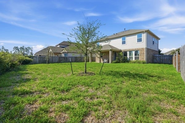 15334 Silver Breeze Lane, Houston, TX 77044 Spacious backyard with lush greenery, perfect for outdoor activities, surrounding a charming two-story home with a mix of brick and siding exterior.