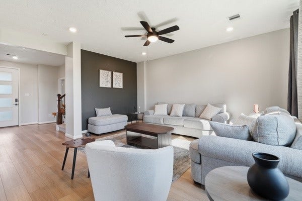 15334 Silver Breeze Lane, Houston, TX 77044 Spacious and modern living room with light wood flooring, a comfortable gray sectional sofa, and stylish accent chairs. A ceiling fan adds a touch of elegance, while large windows provide ample natural light.