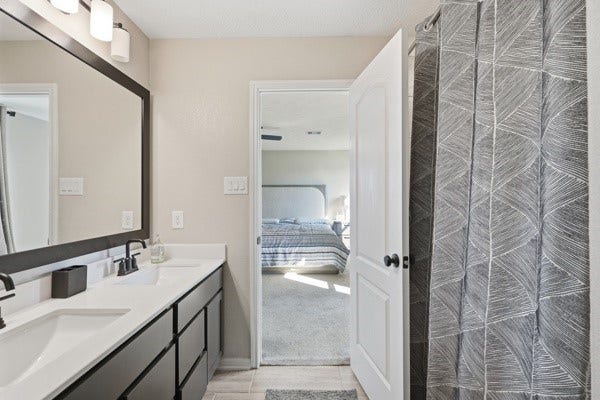 15334 Silver Breeze Lane, Houston, TX 77044 Modern bathroom with a double vanity, sleek fixtures, and a stylish shower curtain, seamlessly connected to a bright bedroom.