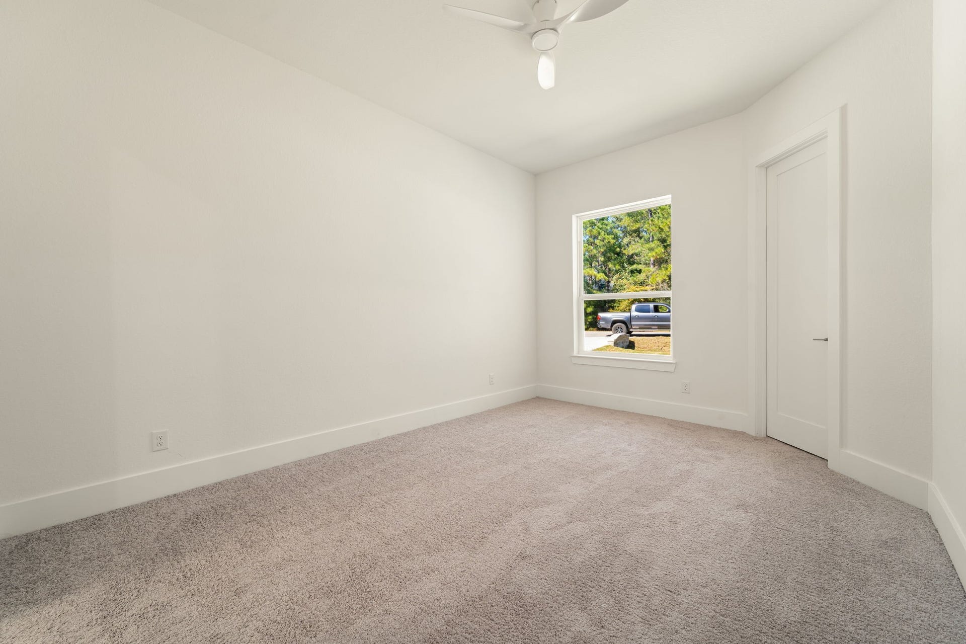 Bright secondary bedroom featuring plush carpeting, neutral finishes, and a peaceful backyard view.