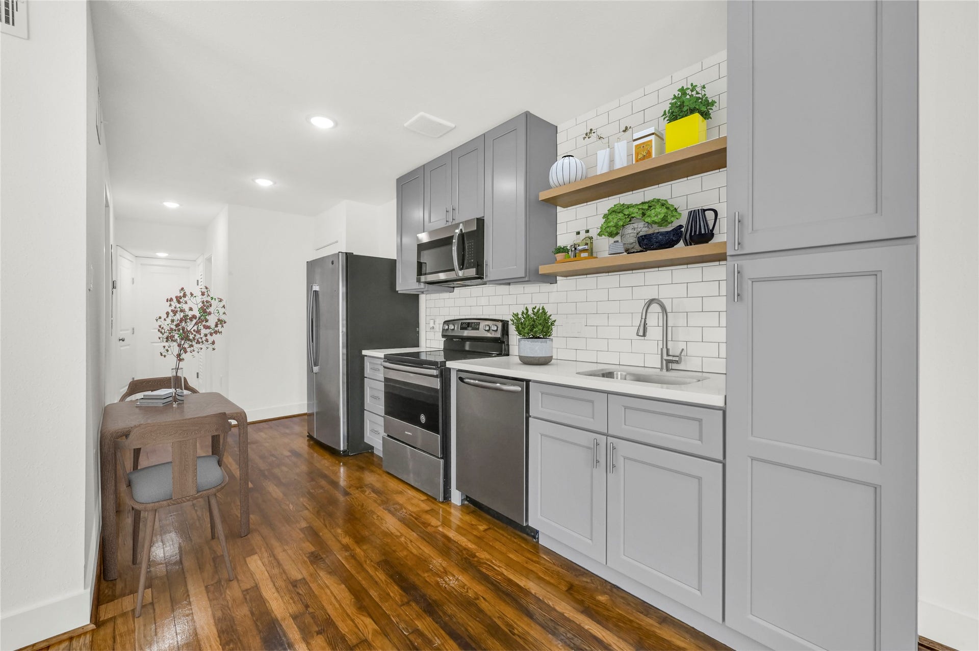 6644 Lawndale Street, #2, Houston, TX 77023 This photo showcases a modern kitchen with sleek gray cabinetry, stainless steel appliances, and a stylish subway tile backsplash. The space features open shelving, ample natural light, complemented by polished wooden floors.