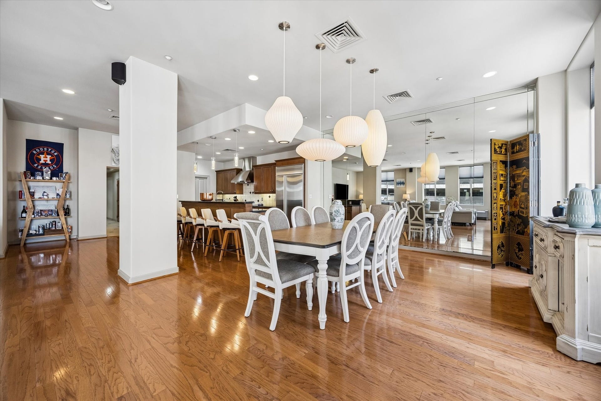 914 Main Street, #801, Houston, TX 77002 Spacious open-concept dining area with elegant hardwood floors, large mirrored wall, and modern pendant lighting, seamlessly flowing into a contemporary kitchen with stainless steel appliances and a breakfast bar.