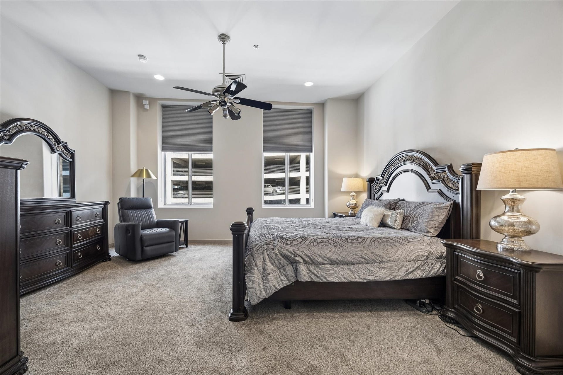 914 Main Street, #801, Houston, TX 77002 Spacious and elegant primary bedroom with plush carpeting, featuring a luxurious bed set, matching dark wood furniture, and modern ceiling fan, all illuminated by ample natural light from large windows.