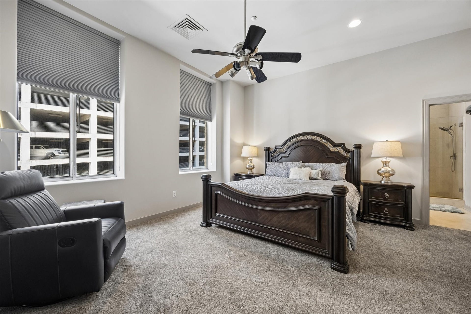 914 Main Street, #801, Houston, TX 77002 Spacious Primary bedroom featuring elegant dark wood furniture, plush carpeting, and ample natural light from large windows, complemented by a cozy seating area and en-suite bathroom access.