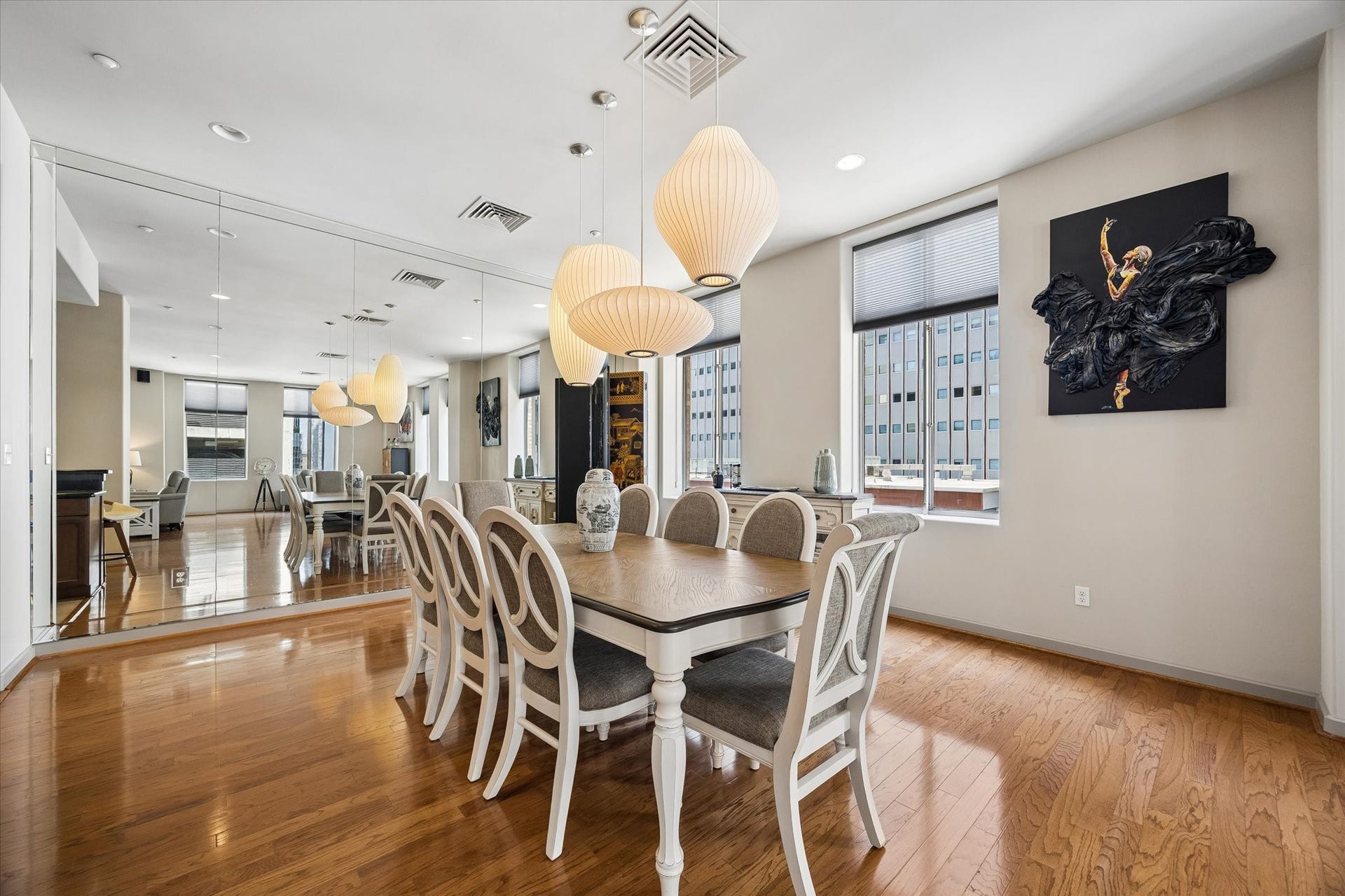 914 Main Street, #801, Houston, TX 77002 Elegant dining area featuring a spacious table with upholstered chairs, accented by stylish pendant lighting and a large mirrored wall that enhances the room's brightness and sense of space.