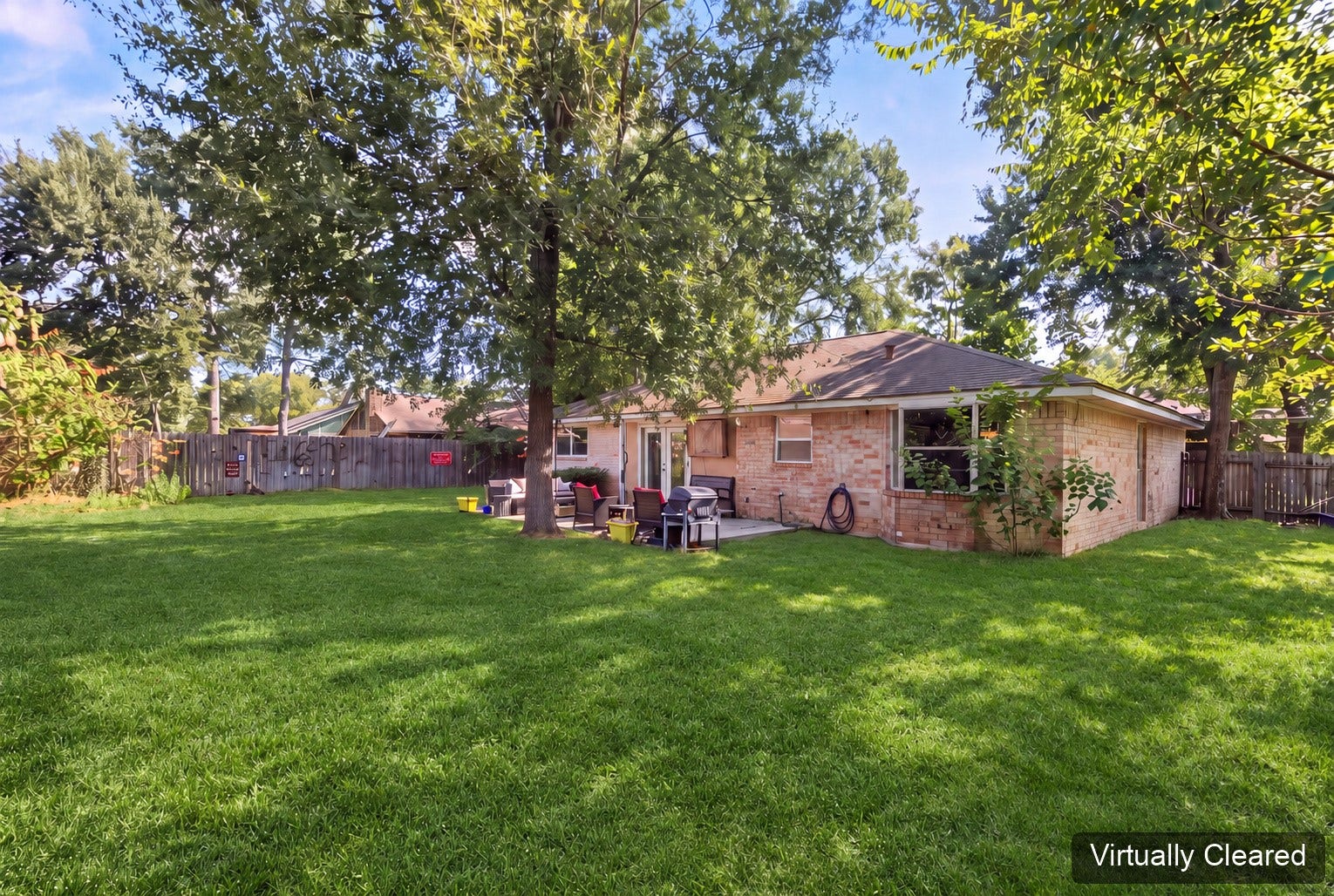 Virtually cleared rear-yard perspective showing the home's brick exterior and tree canopy. The original photo at the end shows existing yard features.