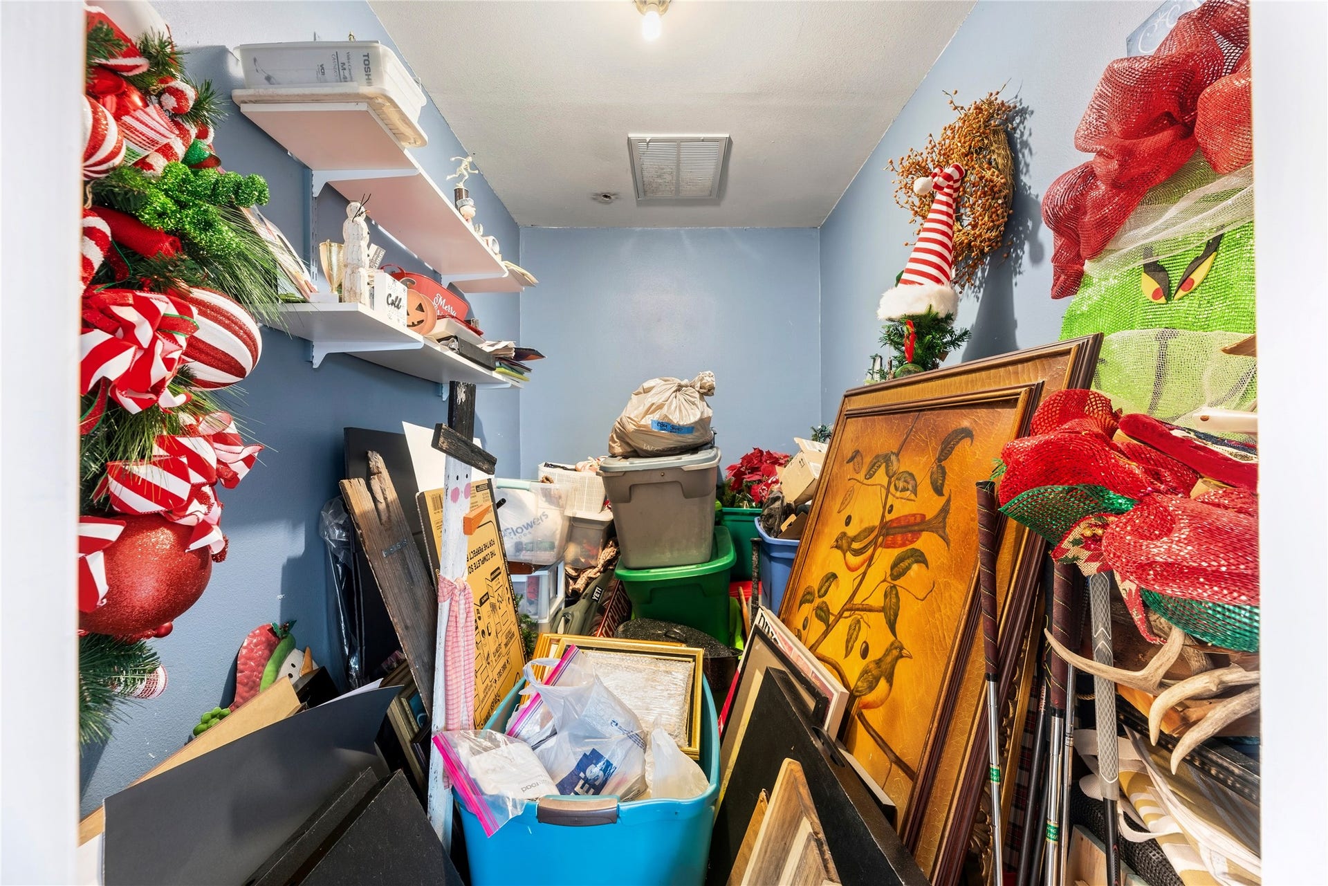 Original bonus storage room inside the garage, connected to the home's HVAC, shown with the existing shelves and stored items. The virtually cleared version earlier in the gallery illustrates the space with those contents removed.