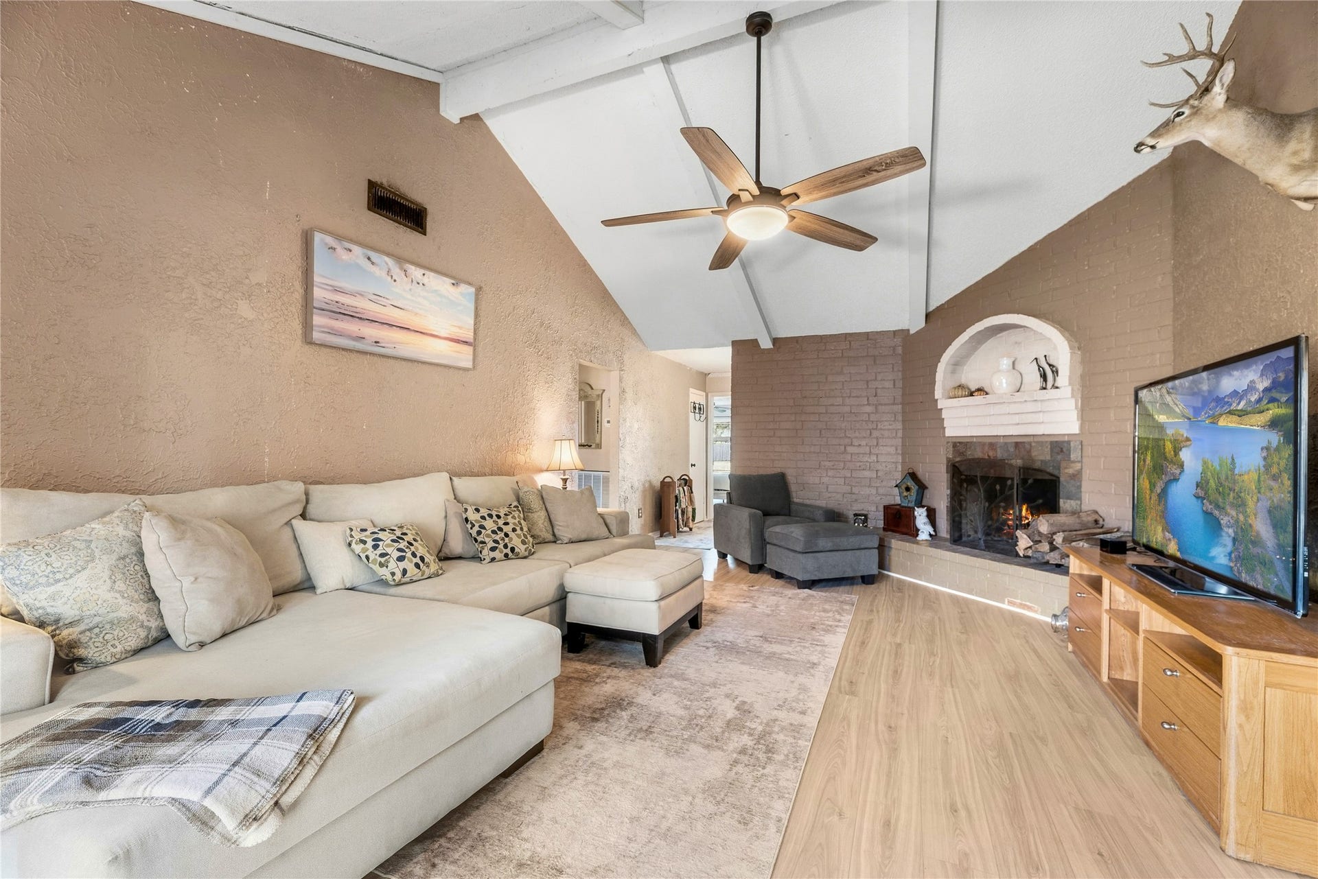 Another living room perspective highlights the vaulted ceiling, ceiling fan, and fireplace focal point.